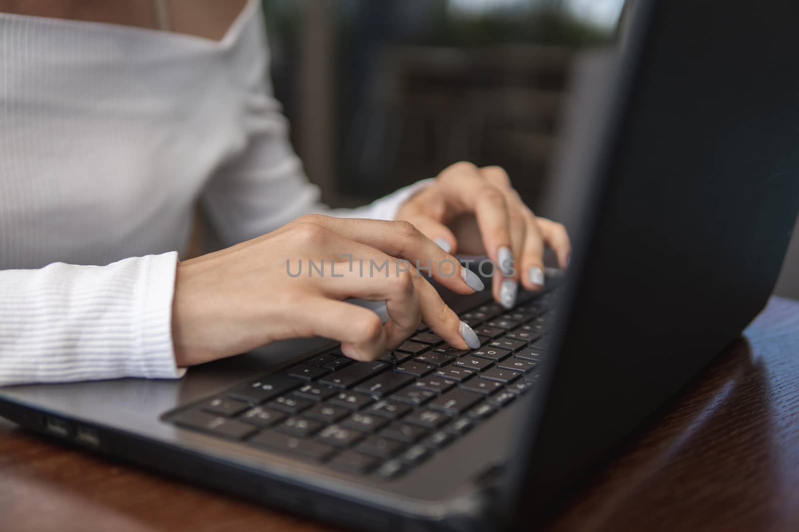 Beautiful young woman in white t-shirt is working on laptop and smiling while sitting outdoors in cafe. Young female using laptop for work. Female freelancer working on laptop in an outdoor cafe