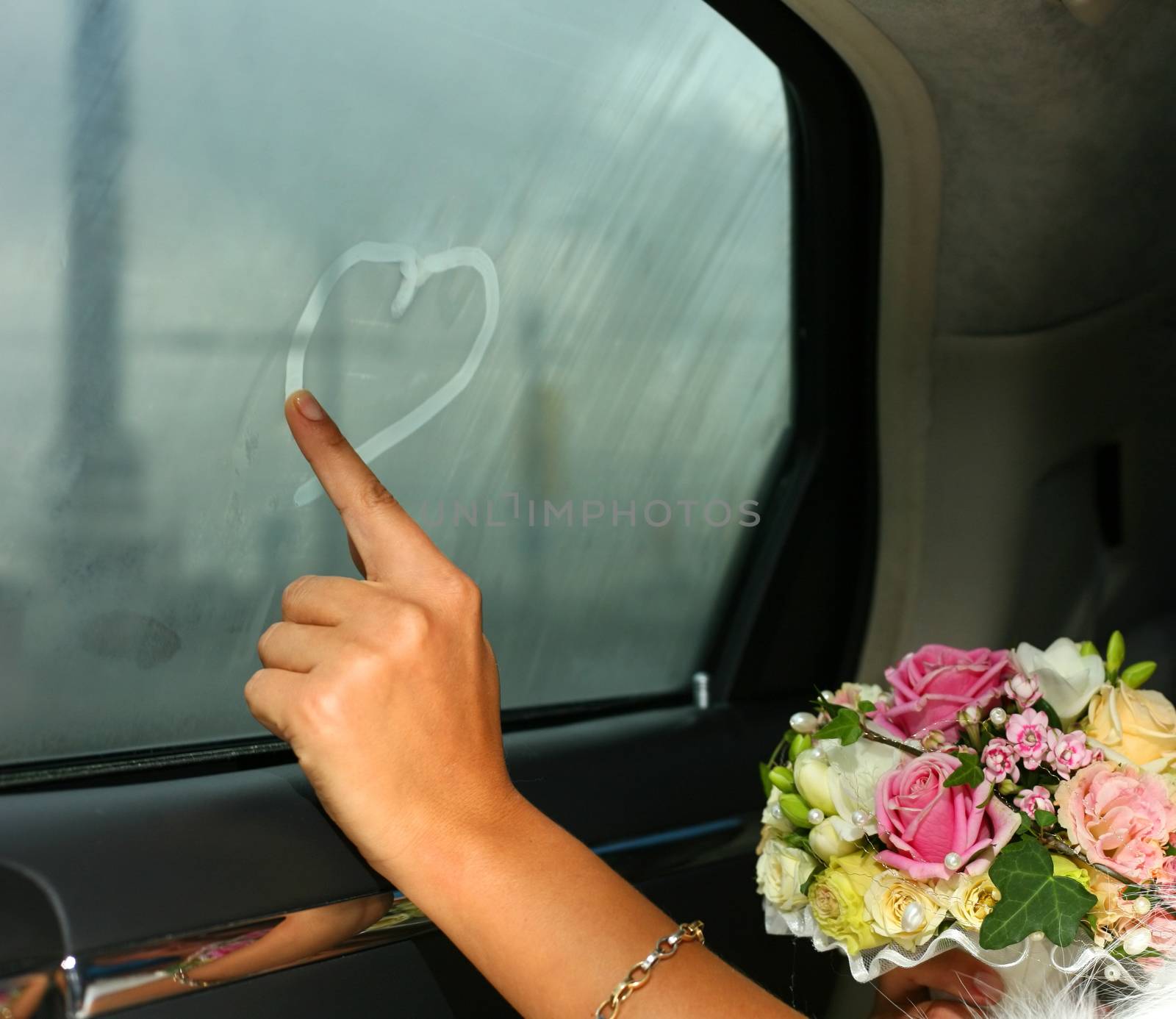 Bride draws heart at a window of the automobile by friday