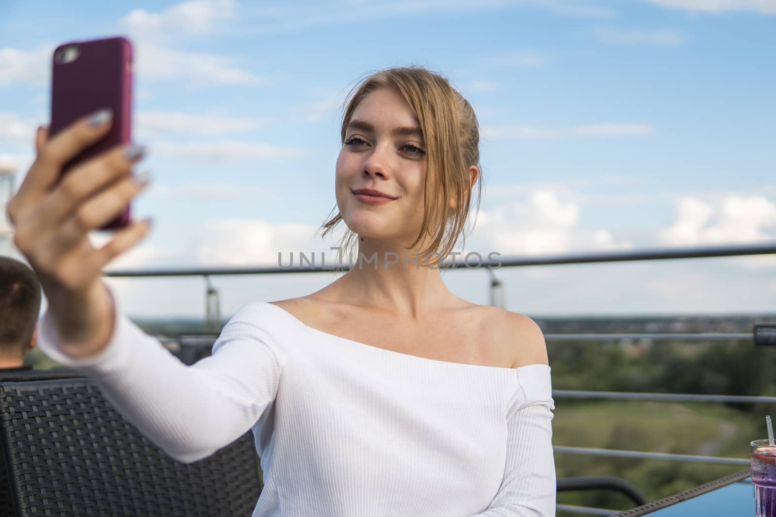 Photo of beautiful lady sitting in cafe and making selfie with a smart phone. Portrait of young smiling student girl make video call from smartphone to her best friend, having break, telling good news, sitting in cafe. by vovsht