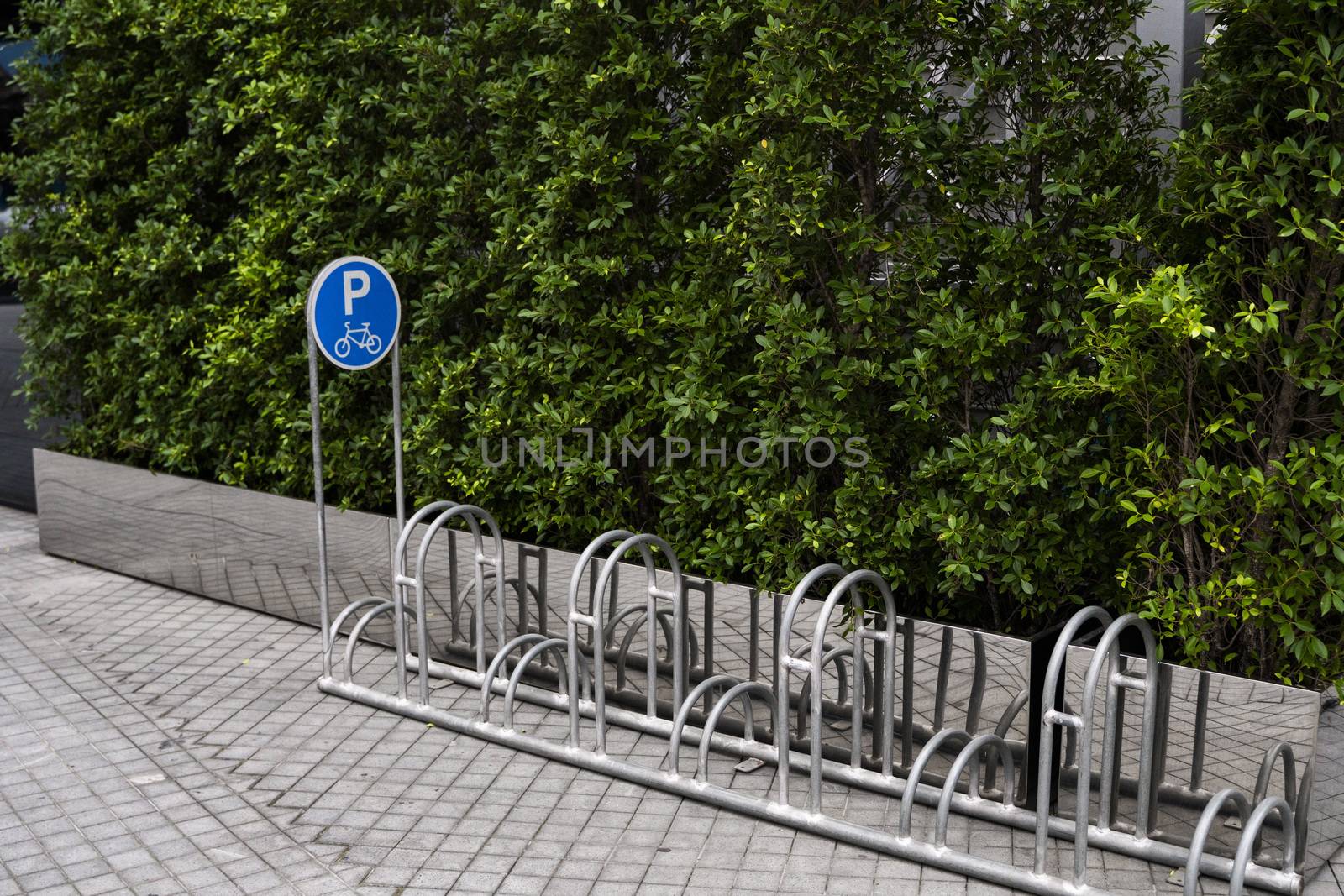 Empty stainless steel bicycle parking rack with a sign of bicycle parking with a green plants on a wall. by vovsht
