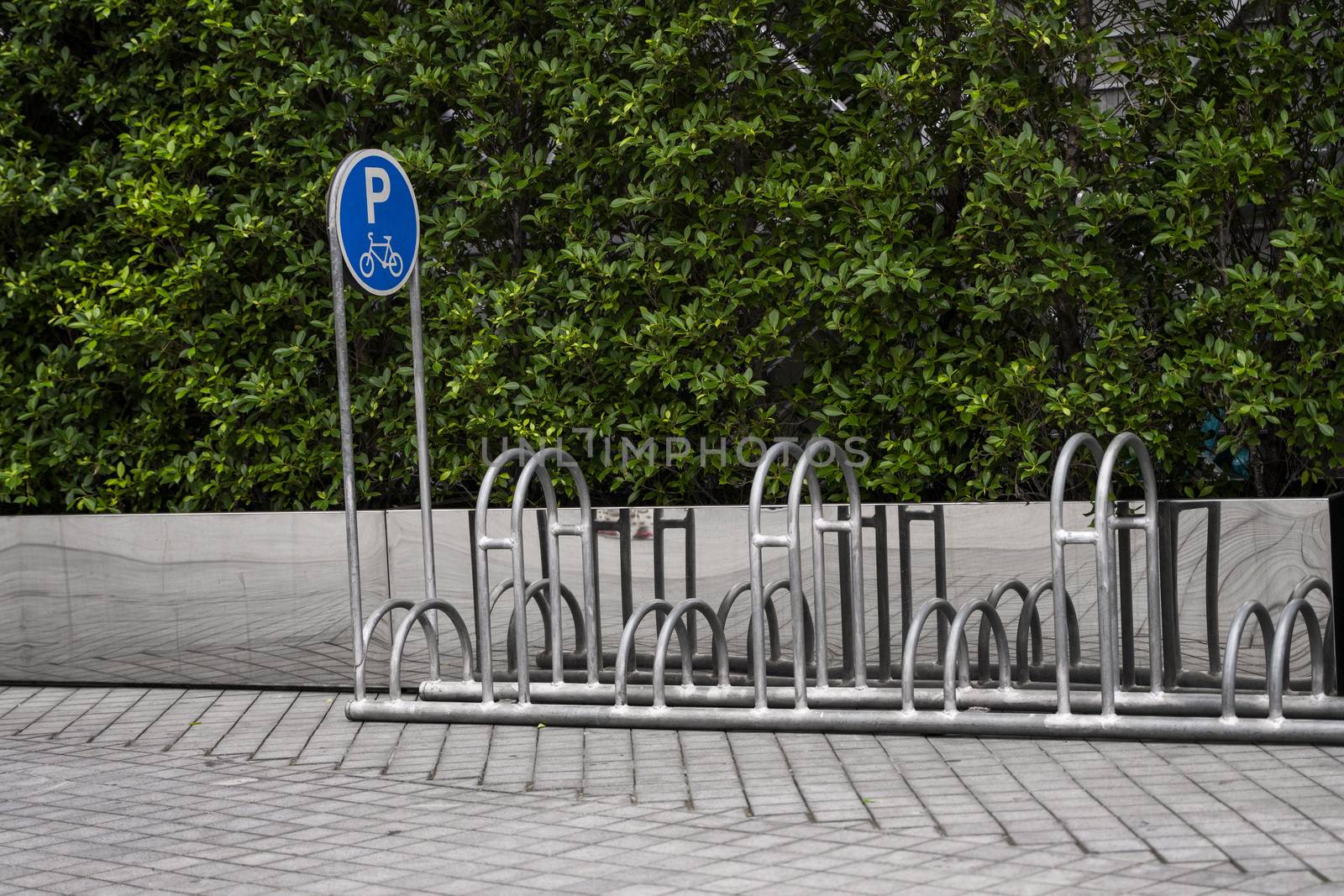 Empty stainless steel bicycle parking rack with a sign of bicycle parking with a green plants on a wall. by vovsht