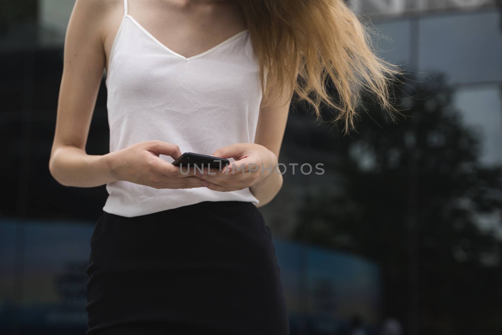 A portrait of a beautiful woman texting a message or reading white standing on a street. by vovsht