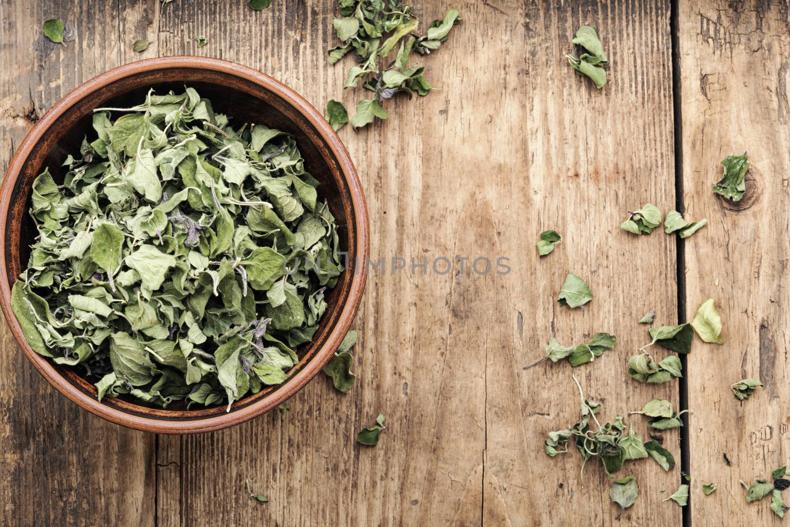 Bowl of dried oregano leaves on wooden background