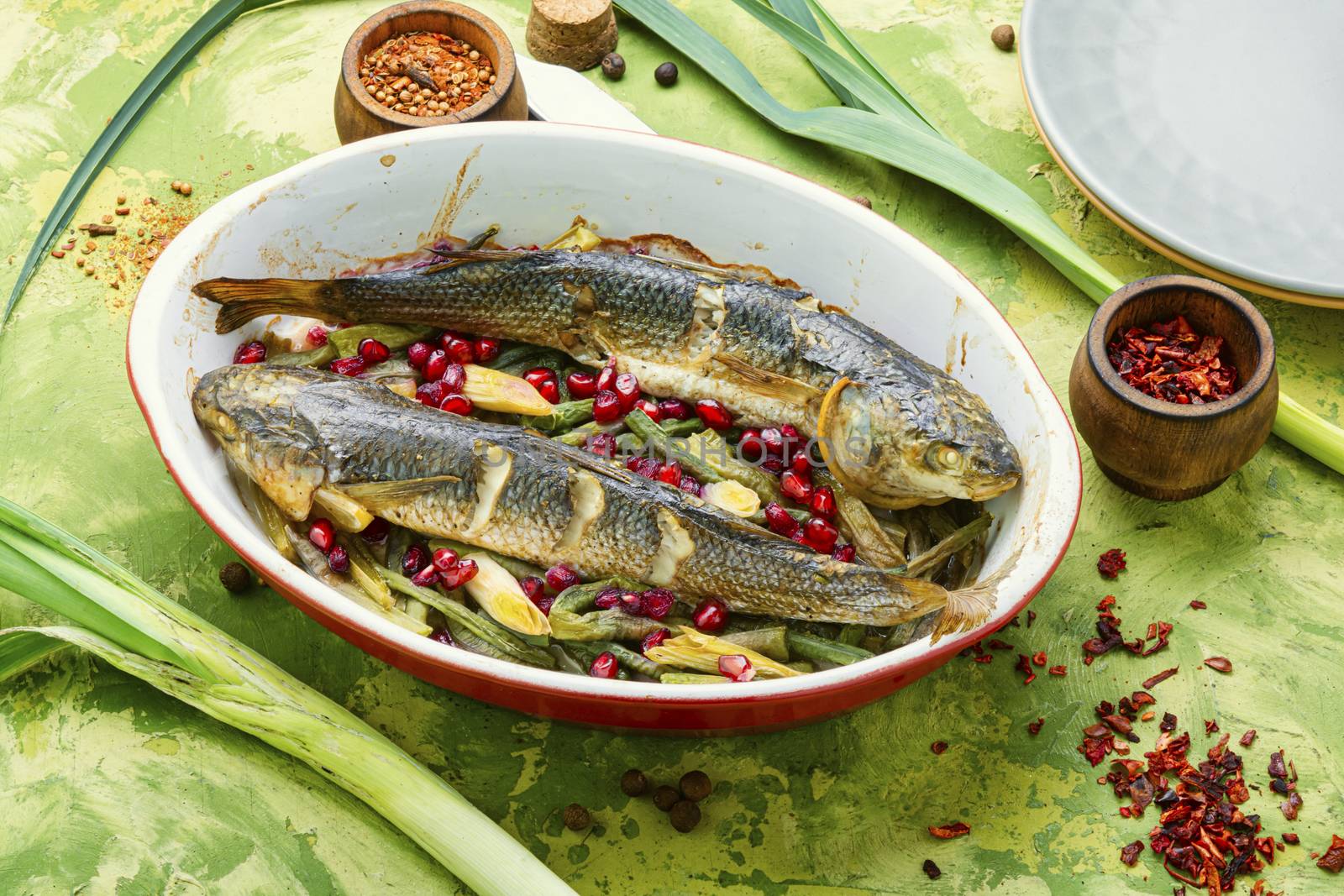 Pelengas baked with vegetables and pomegranate.Cooked roasted fish in a baking dish.