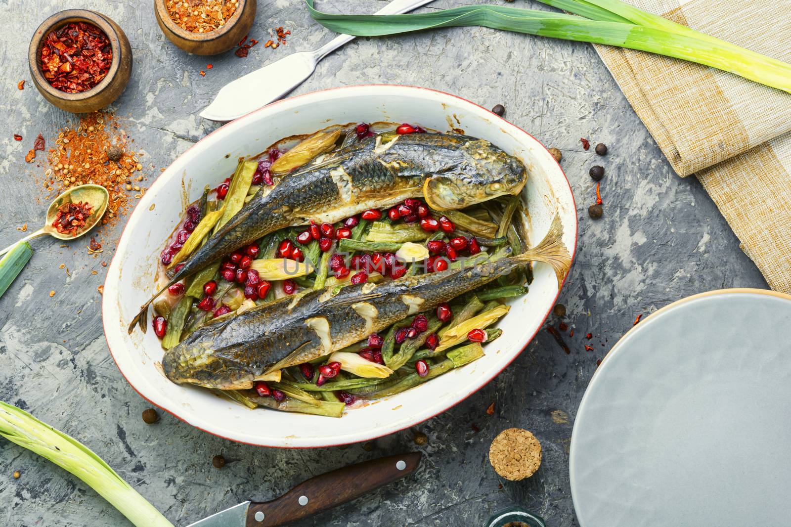 Pelengas baked with vegetables and pomegranate.Cooked roasted fish in a baking dish.