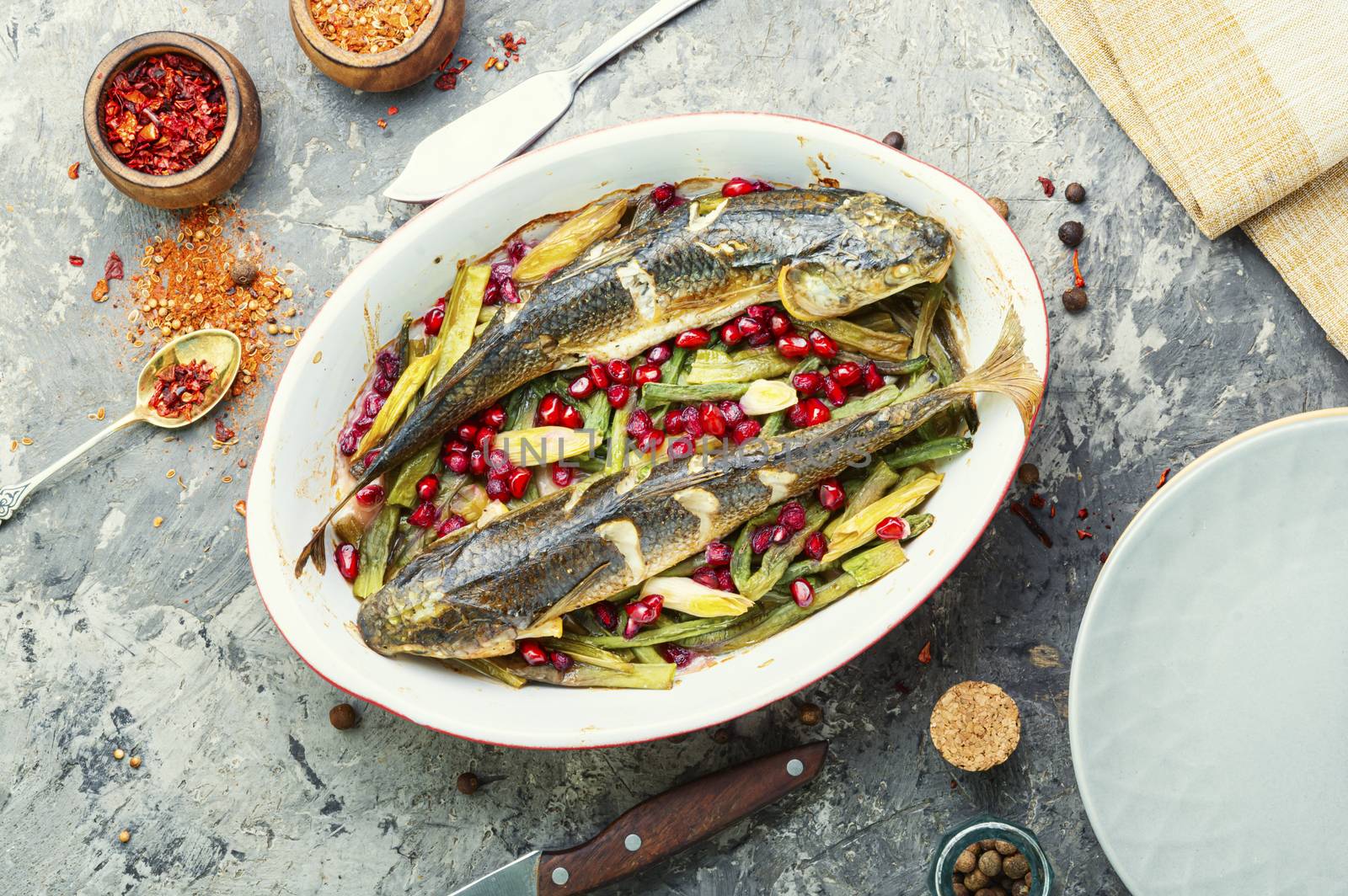 Pelengas baked with vegetables and pomegranate.Cooked roasted fish in baking dish.