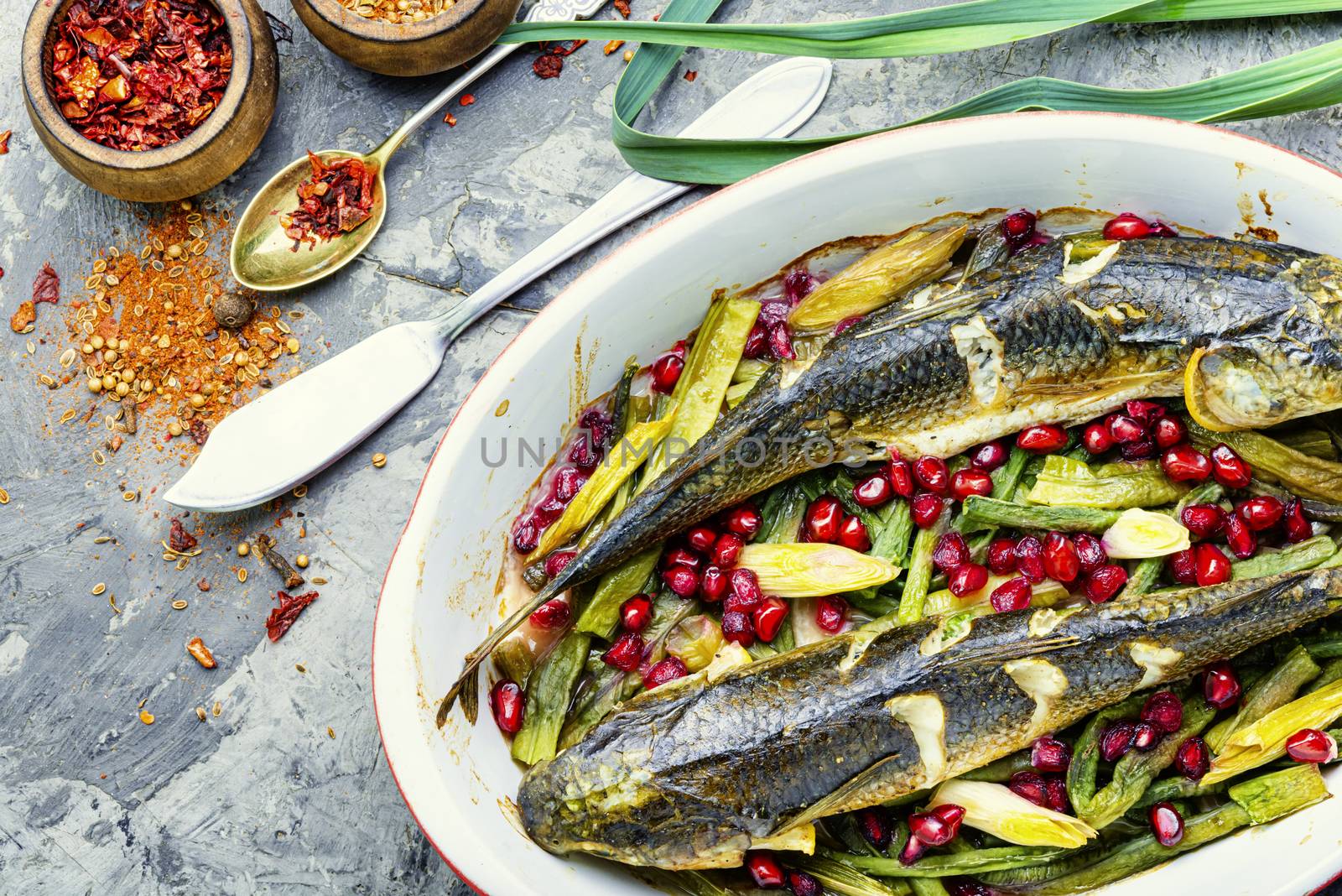 Pelengas baked with vegetables and pomegranate.Cooked roasted fish in a baking dish.