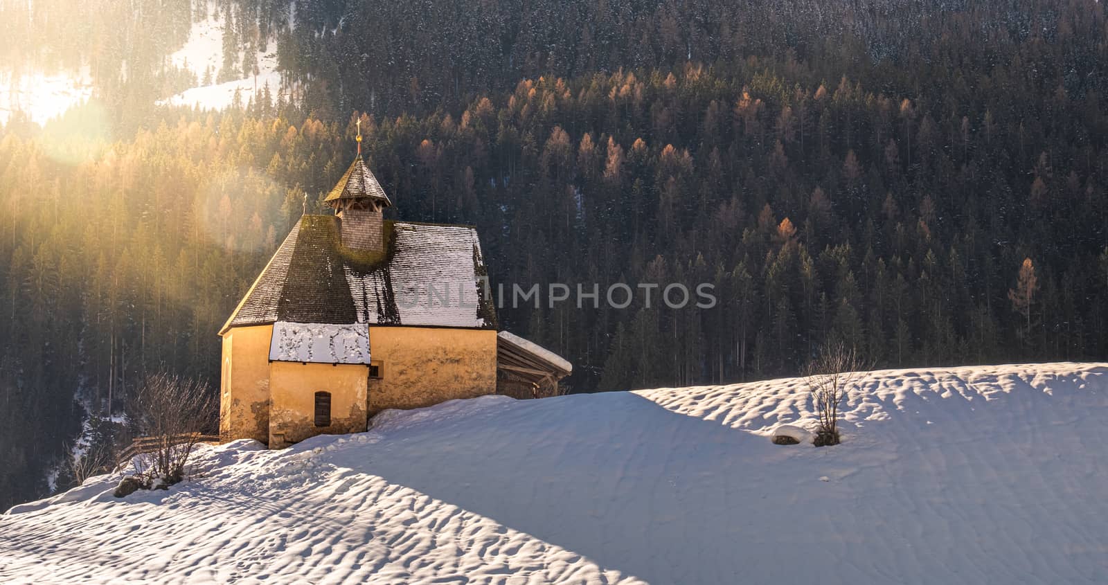 mountain landscape, panoramic snow slope with church in winter day with sun flare and lens flare by LucaLorenzelli