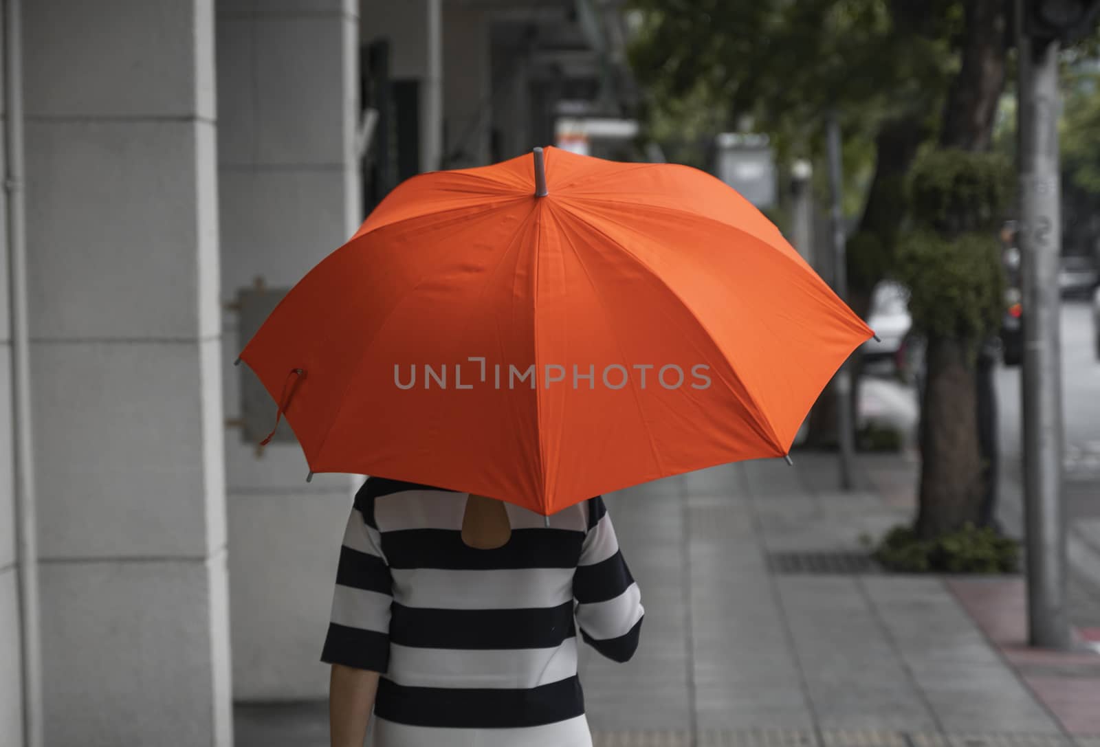 Back view of woman with orange umbrella walking on a street