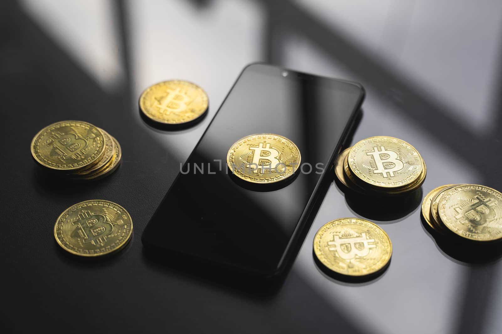 Golden bitcoin coin on a smartphone with a lot of bitcoins coins on a table. Virtual cryptocurrency concept. Mining of bitcoins online bussiness. Bitcoins trading. by vovsht