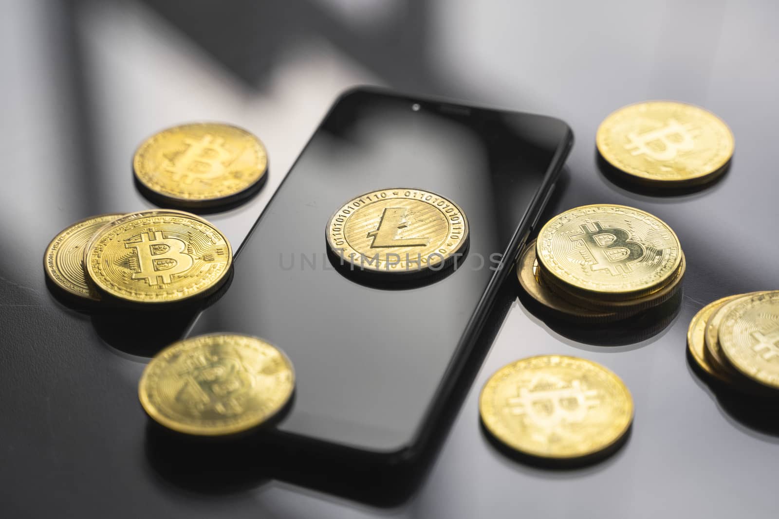 Golden litecoin coin on a smartphone with a lot of bitcoins coins on a table. Virtual cryptocurrency concept. Mining of bitcoins online bussiness. Bitcoins trading