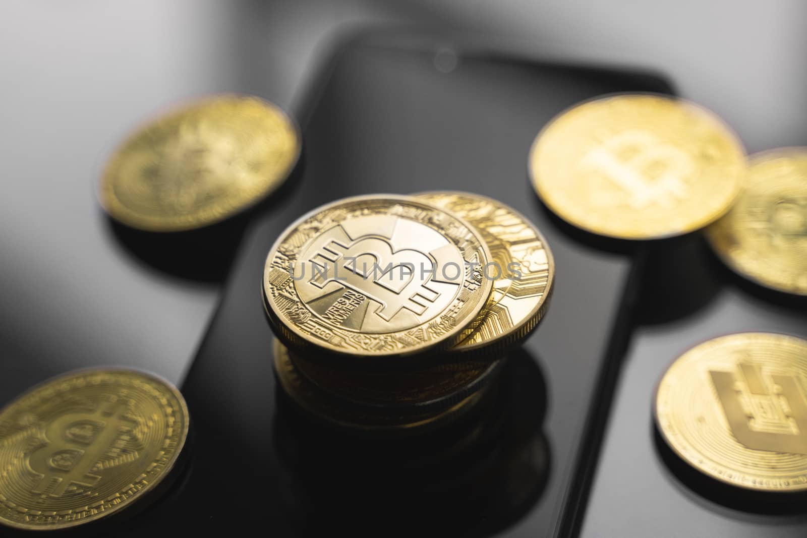 Golden bitcoin coin on a smartphone with a lot of bitcoins coins on a table. Virtual cryptocurrency concept. Mining of bitcoins online bussiness. Bitcoins trading. by vovsht