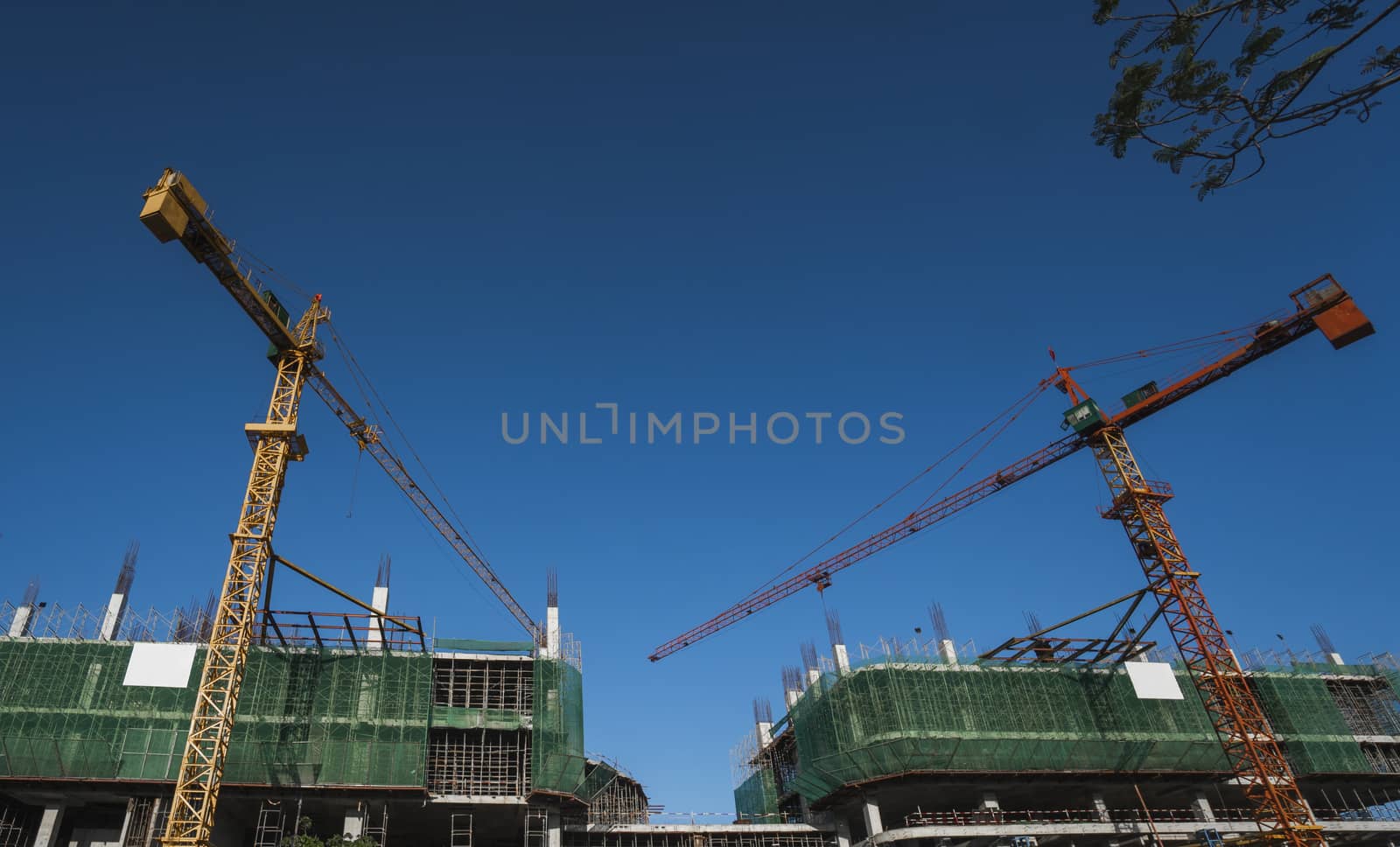 Cranes and building construction site against blue sky. Metal construction of unfinished building on construction. Tower Crane use for building of multi storage building