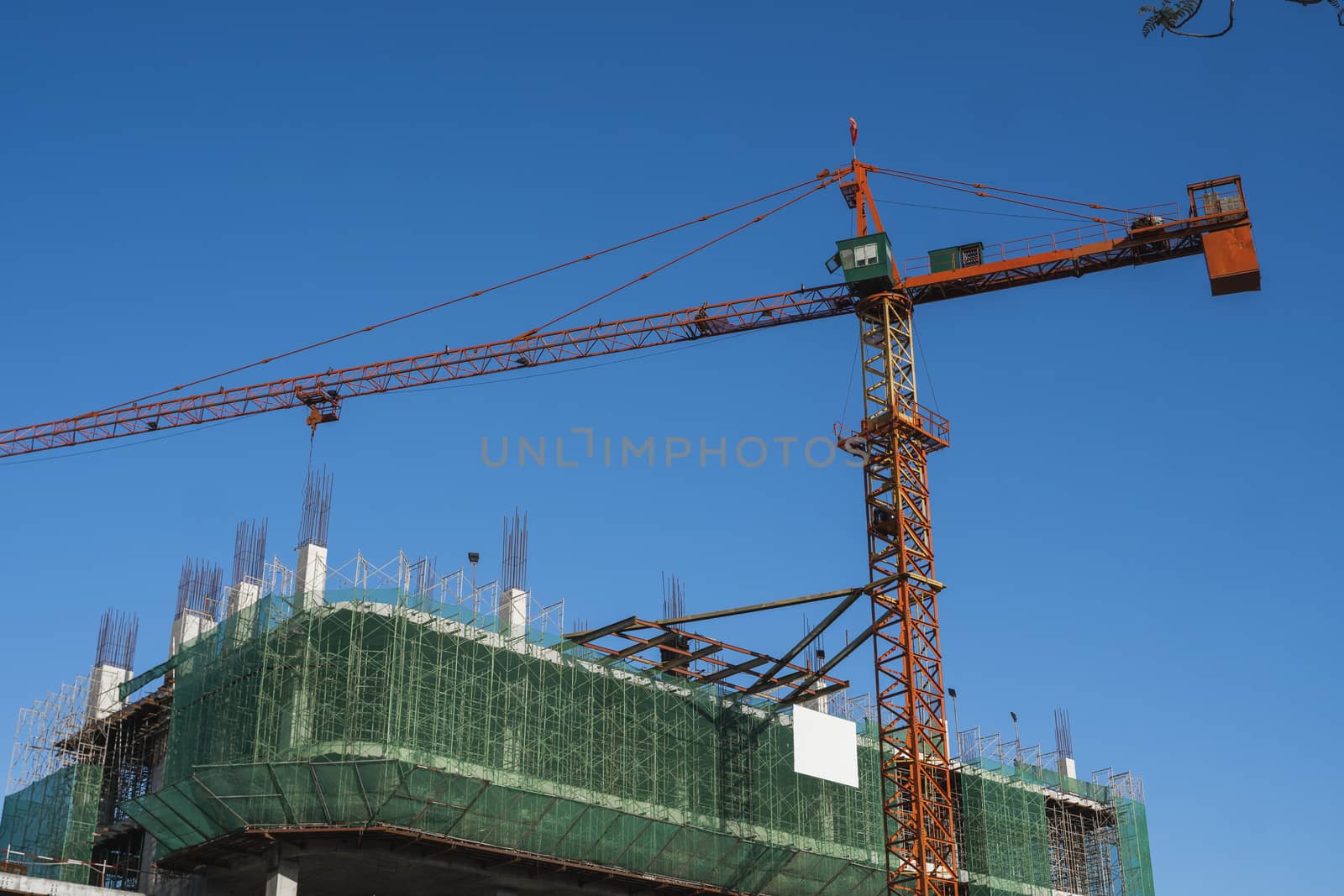 Crane and building construction site against blue sky. Metal construction of unfinished building on construction. Tower Crane use for building of multi storage building. by vovsht