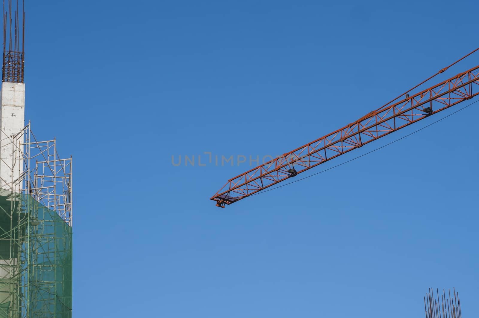 Crane and building construction site against blue sky. Metal construction of unfinished building on construction. Tower Crane use for building of multi storage building