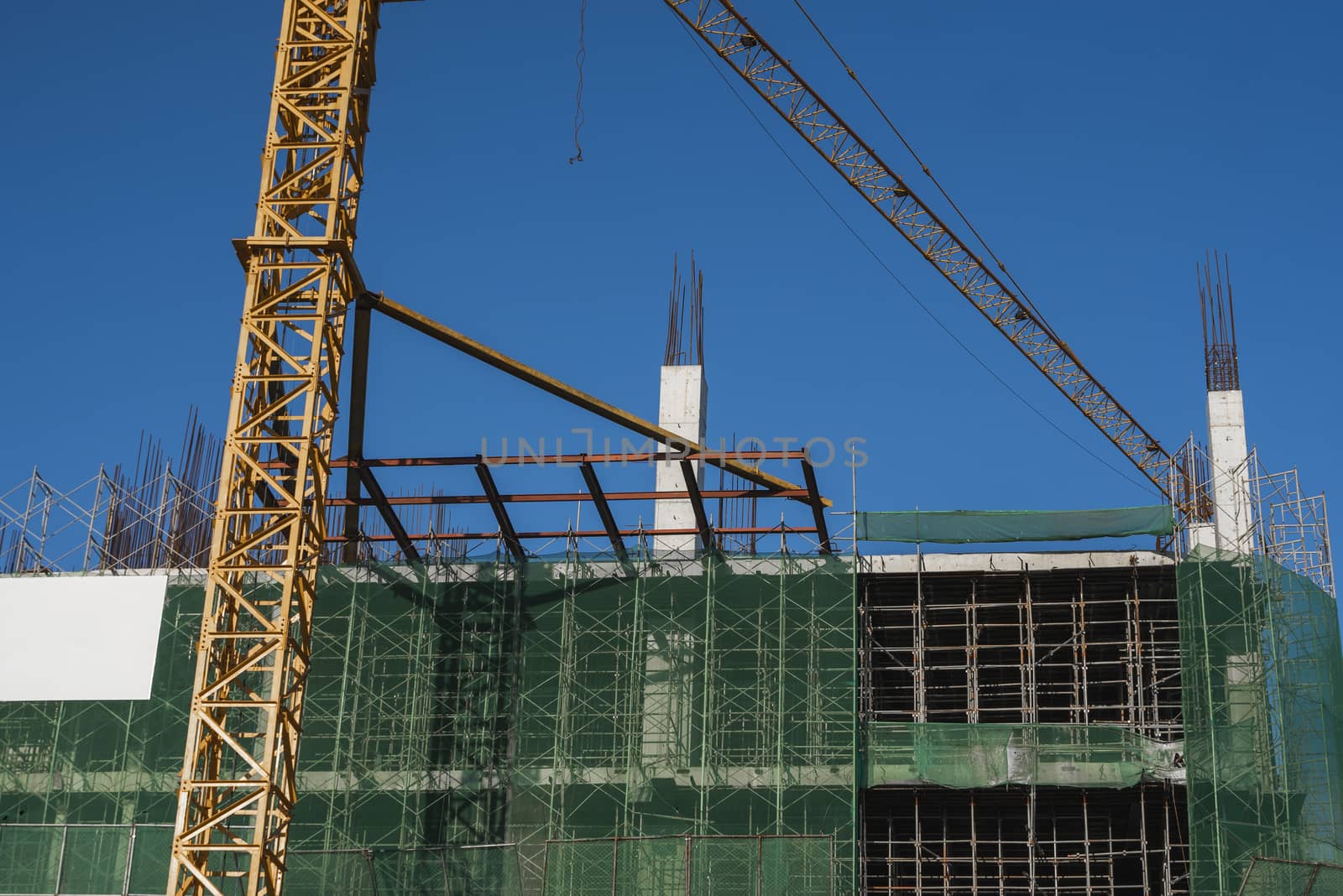 Crane and building construction site against blue sky. Metal construction of unfinished building on construction. Tower Crane use for building of multi storage building. by vovsht