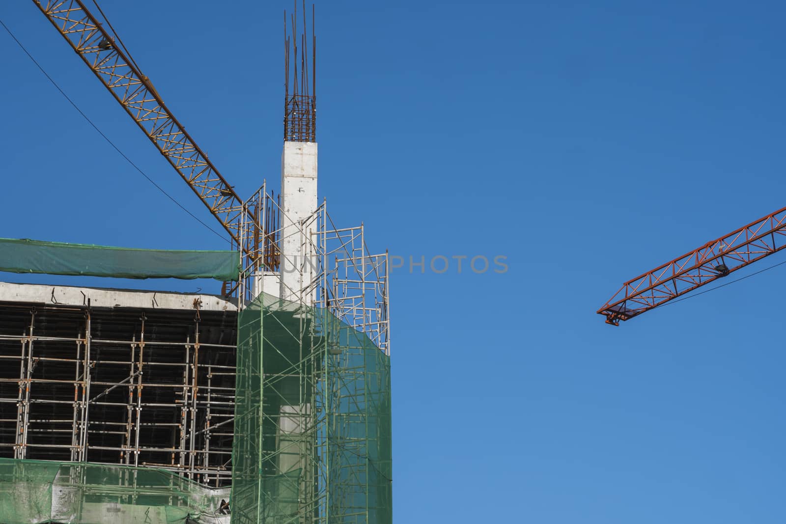 Cranes and building construction site against blue sky. Metal construction of unfinished building on construction. Tower Crane use for building of multi storage building. by vovsht