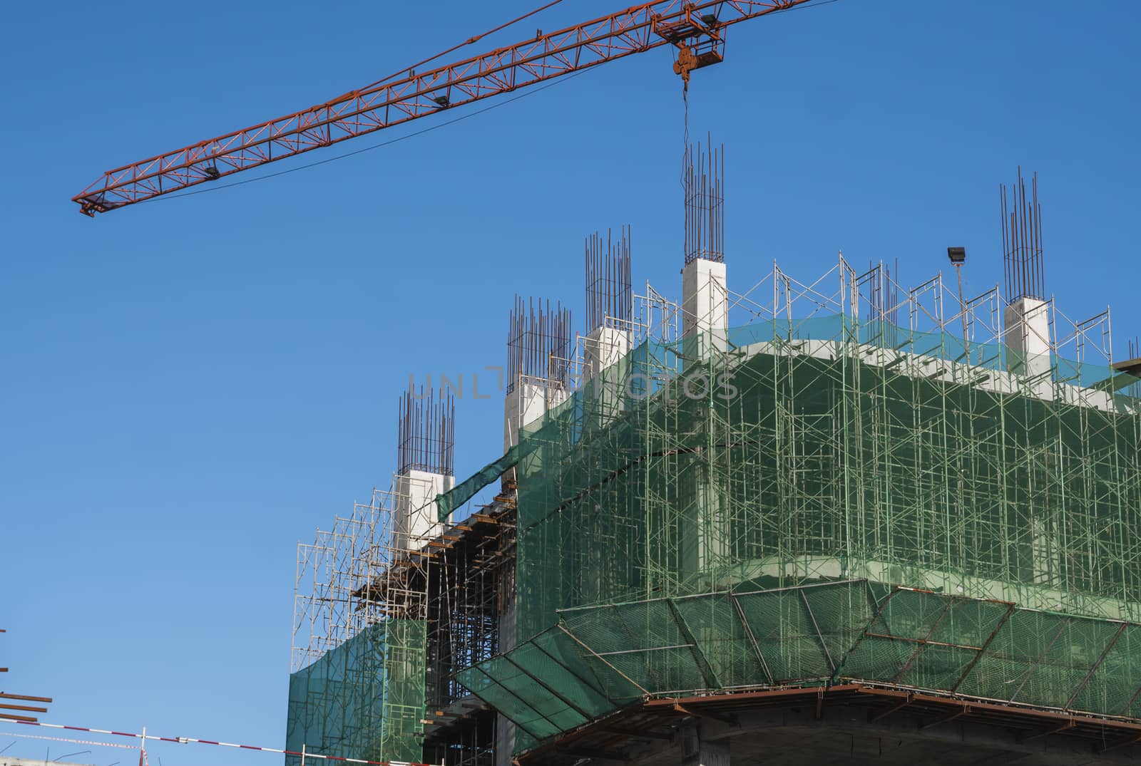 Crane and building construction site against blue sky. Metal construction of unfinished building on construction. Tower Crane use for building of multi storage building. by vovsht