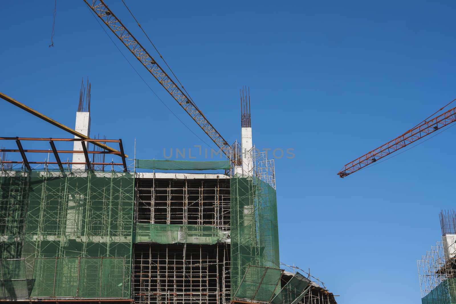 Crane and building construction site against blue sky. Metal construction of unfinished building on construction. Tower Crane use for building of multi storage building. by vovsht