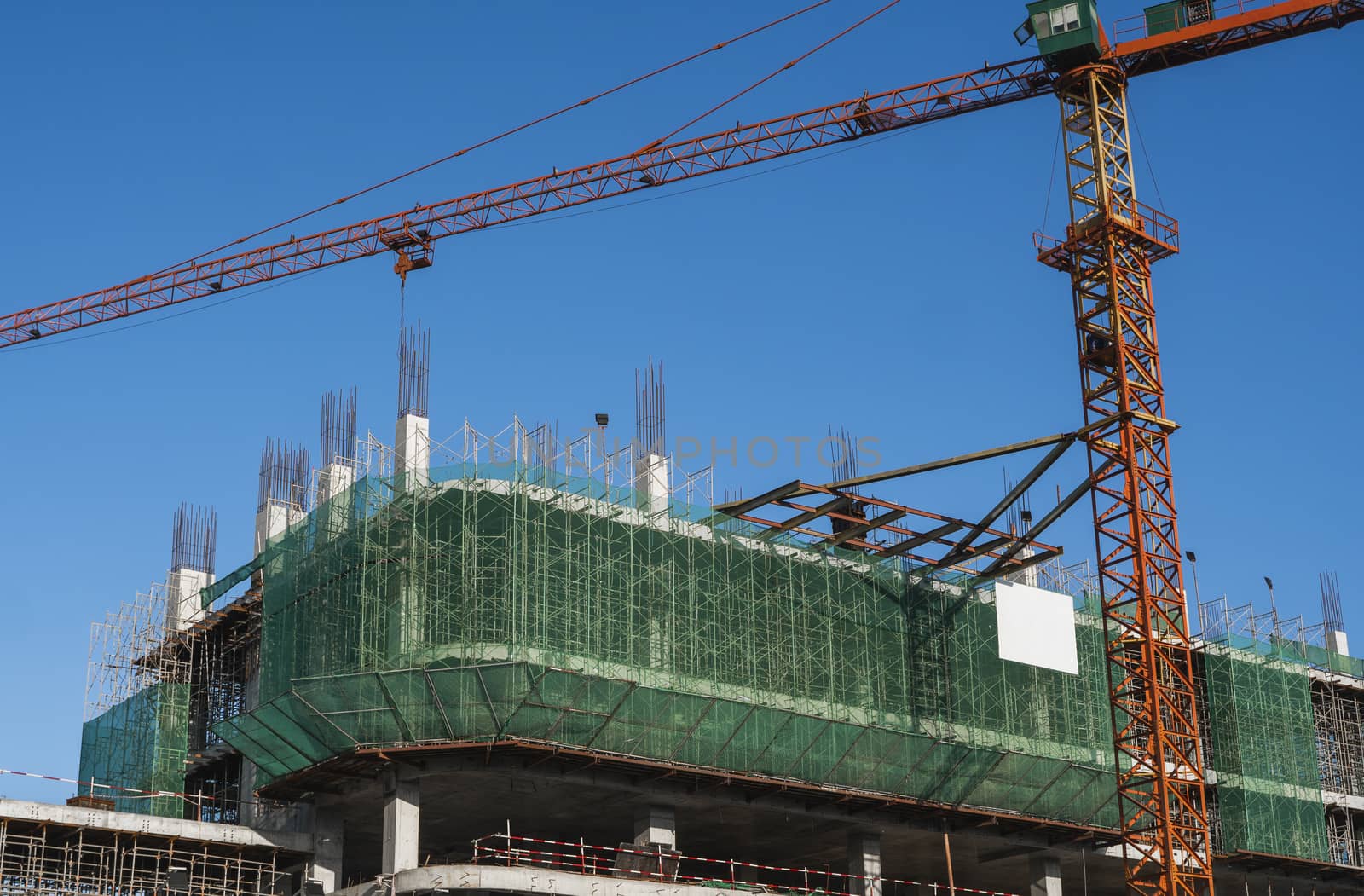 Crane and building construction site against blue sky. Metal construction of unfinished building on construction. Tower Crane use for building of multi storage building. by vovsht