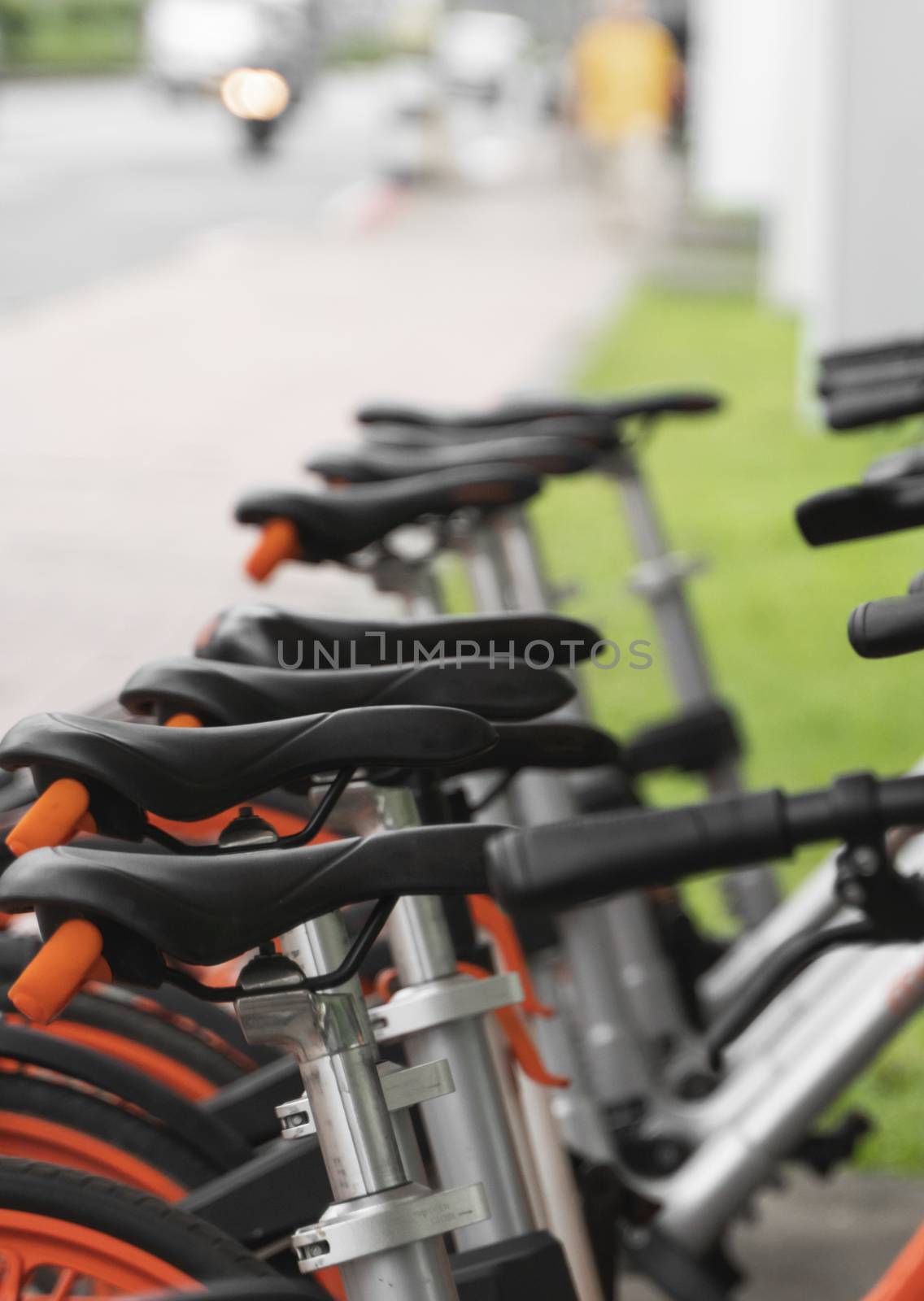Street transportation orange hybrid rent bicycles with electronic form of payment for traveling around the city stand in row on rental network parking lot waiting for cyclists to make bike trip. by vovsht