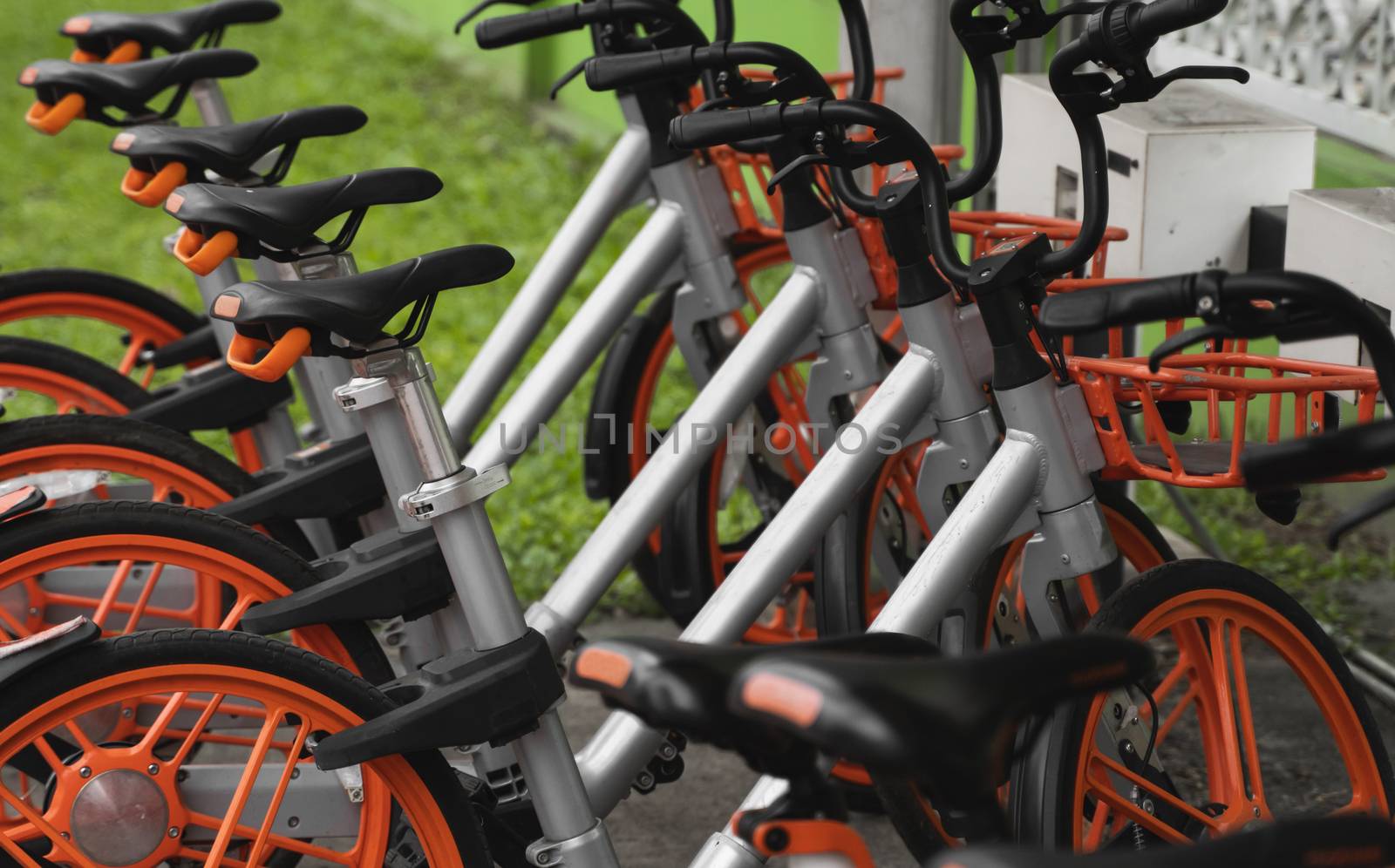 Street transportation orange hybrid rent bicycles with electronic form of payment for traveling around the city stand in row on rental network parking lot waiting for cyclists to make bike trip. by vovsht