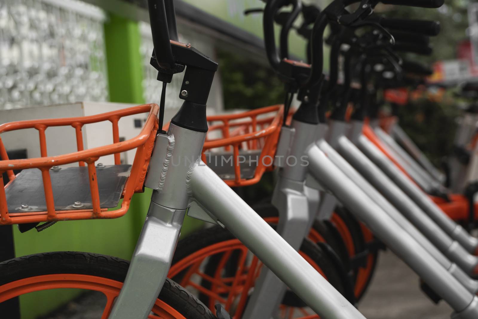 Street transportation orange hybrid rent bicycles with electronic form of payment for traveling around the city stand in row on rental network parking lot waiting for cyclists to make bike trip. by vovsht