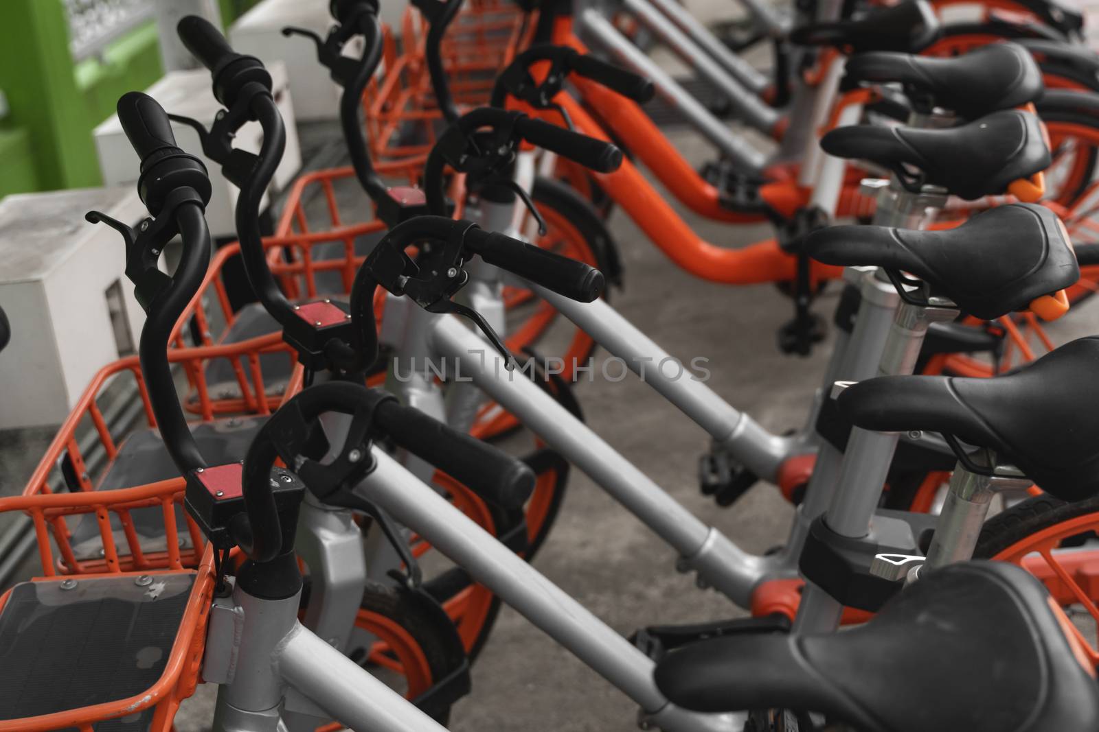 Street transportation orange hybrid rent bicycles with electronic form of payment for traveling around the city stand in row on rental network parking lot waiting for cyclists to make bike trip. by vovsht