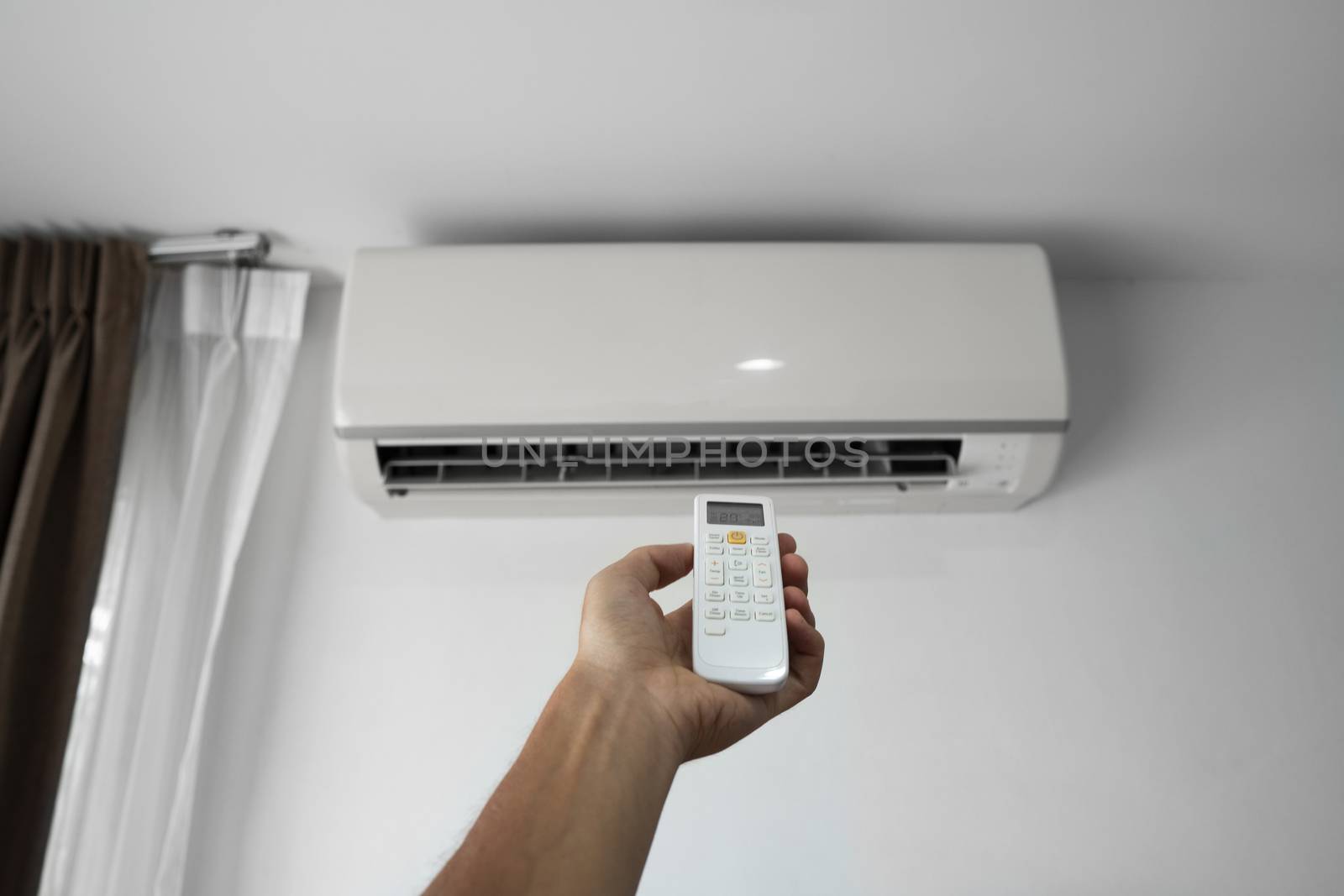 Man's hand using remote controler. Hand holding rc and adjusting temperature of air conditioner mounted on a white wall. Indooor comfort temperature. Health concepts and energy savings