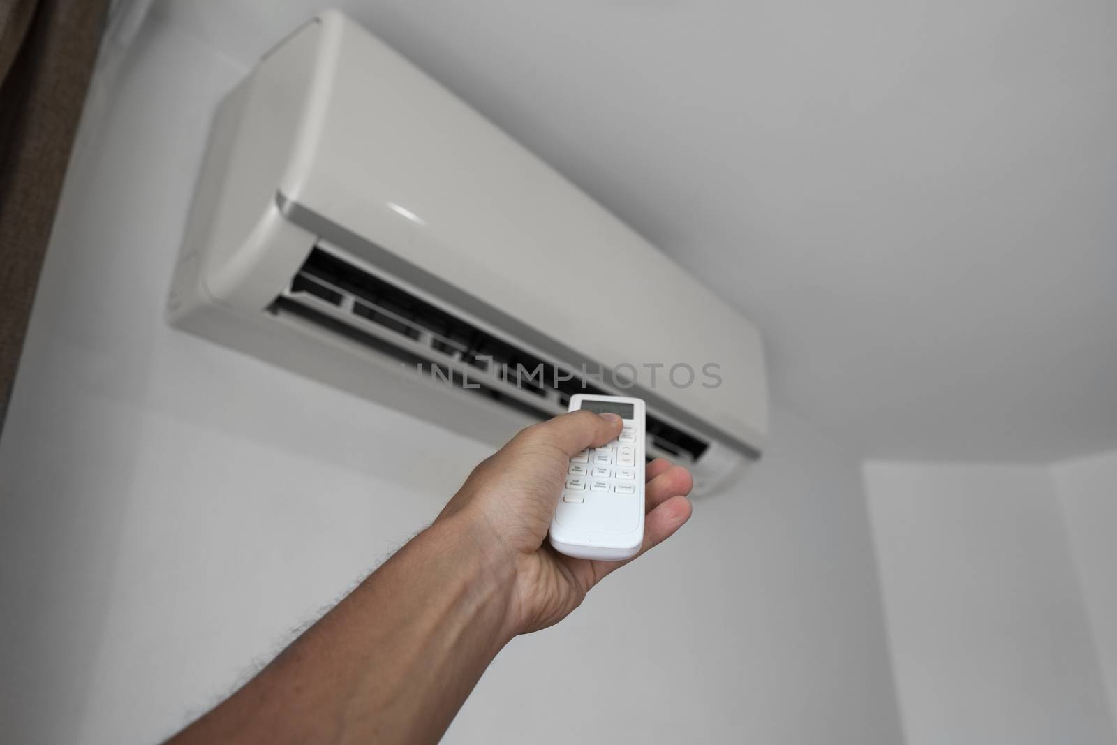 Man's hand using remote controler. Hand holding rc and adjusting temperature of air conditioner mounted on a white wall. Indooor comfort temperature. Health concepts and energy savings. by vovsht