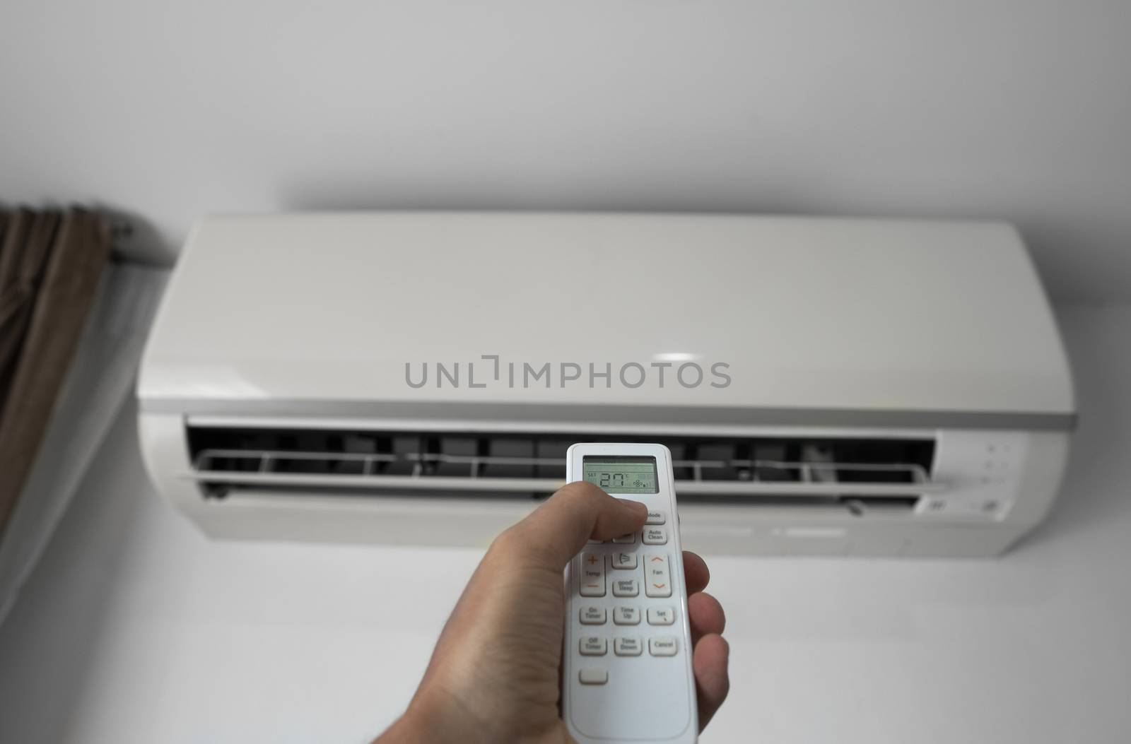 Man's hand using remote controler. Hand holding rc and adjusting temperature of air conditioner mounted on a white wall. Indooor comfort temperature. Health concepts and energy savings. by vovsht