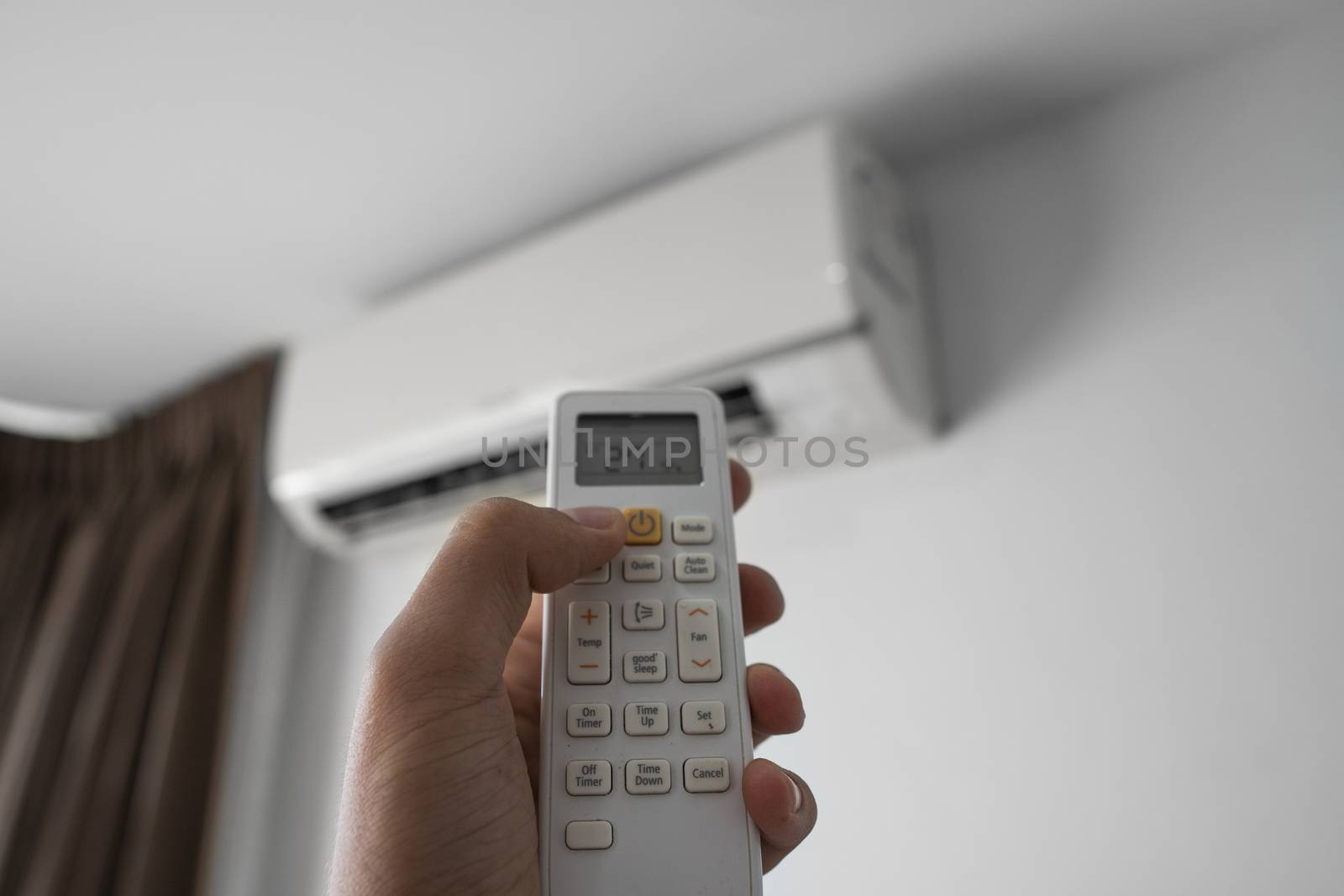 Man's hand using remote controler. Hand holding rc and adjusting temperature of air conditioner mounted on a white wall. Indooor comfort temperature. Health concepts and energy savings