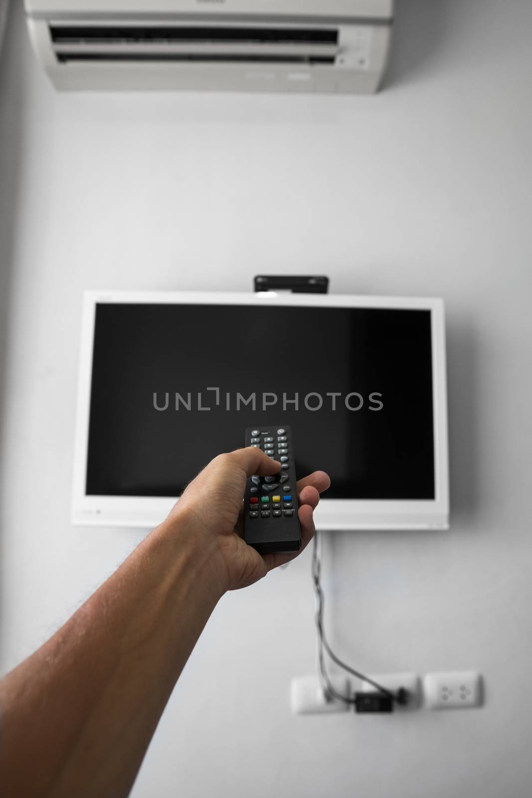 The man with the remote control in hand want switch on the TV and presses the button on the remote control. Remote control in hand closeup