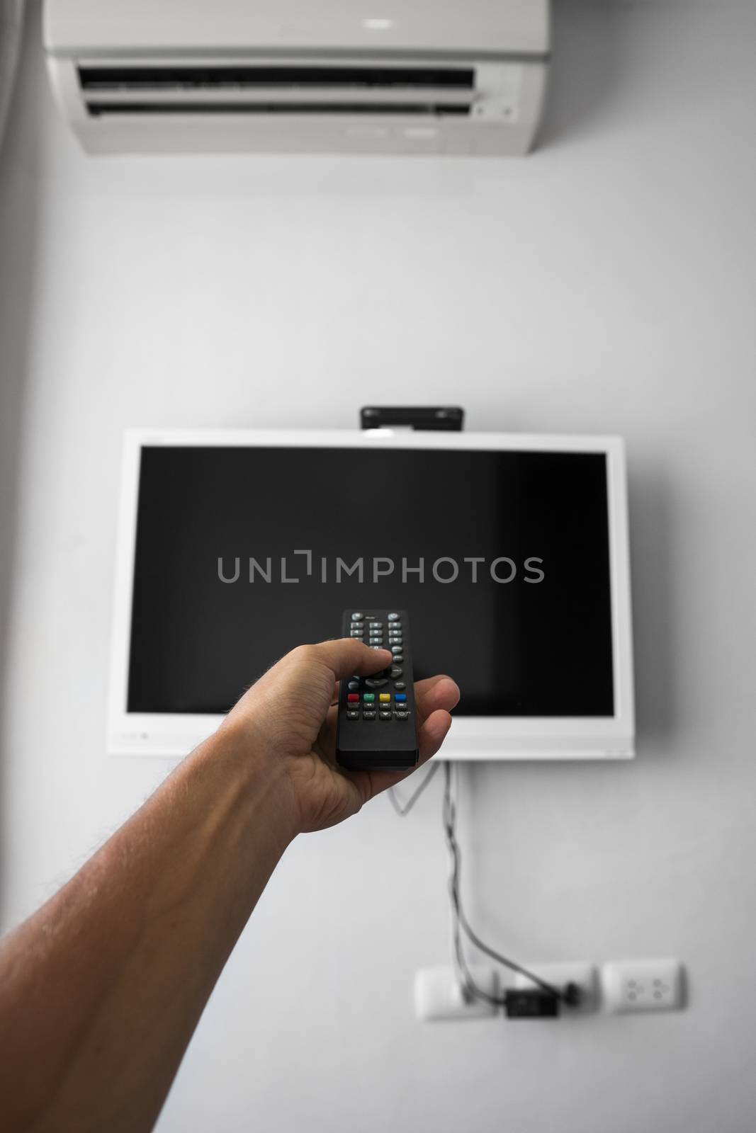The man with the remote control in hand want switch on the TV and presses the button on the remote control. Remote control in hand closeup. by vovsht