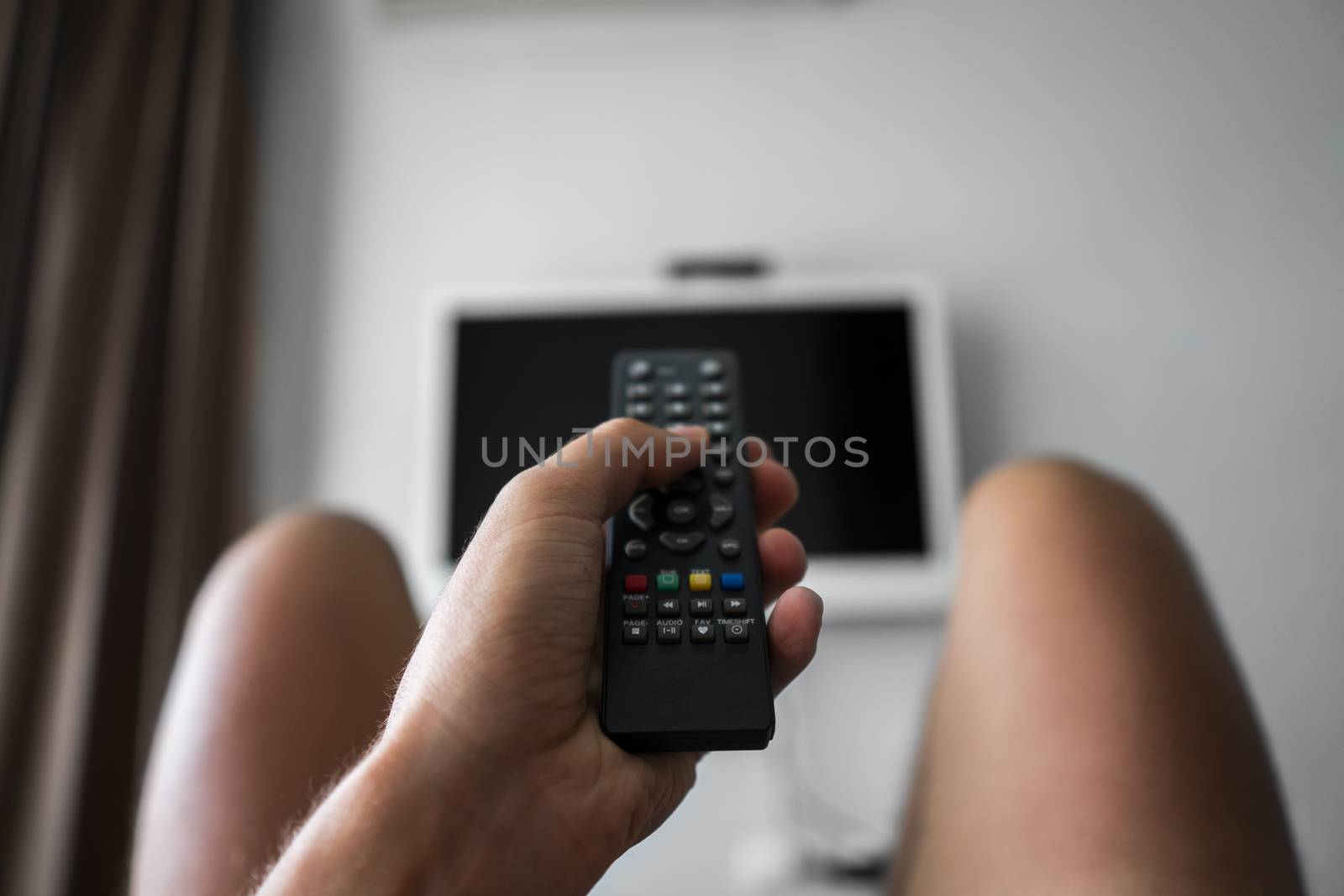 The man with the remote control in hand want switch on the TV and presses the button on the remote control. Remote control in hand closeup