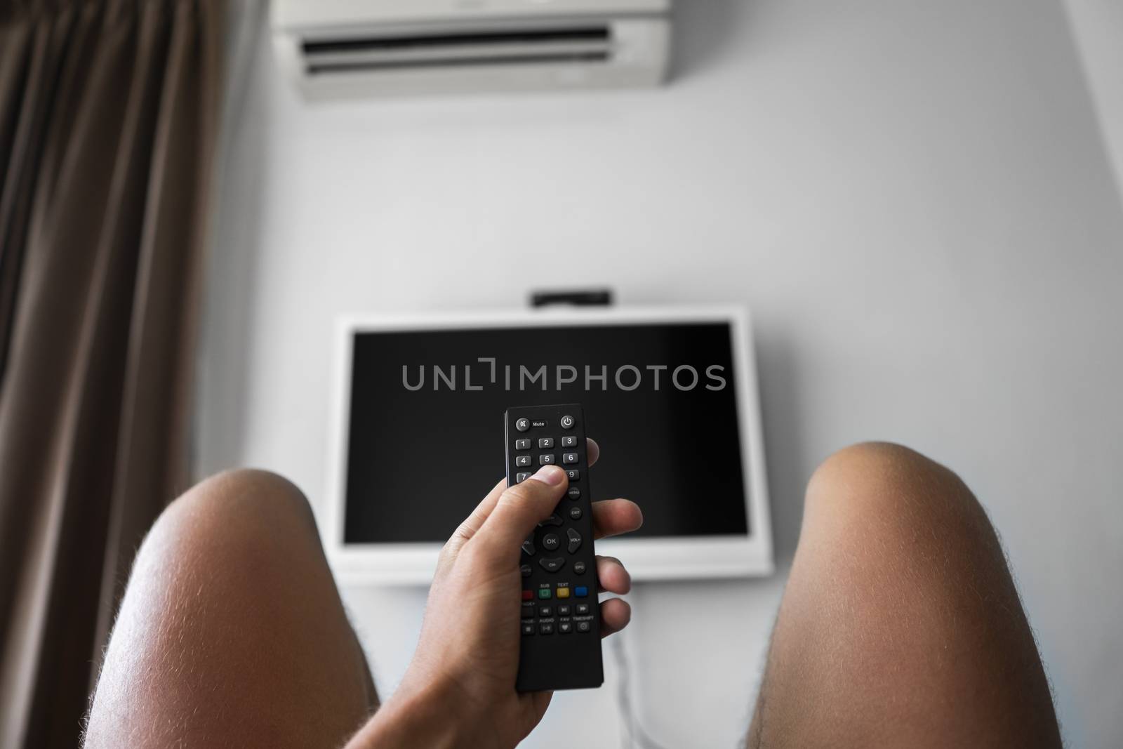 The man with the remote control in hand want switch on the TV and presses the button on the remote control. Remote control in hand closeup