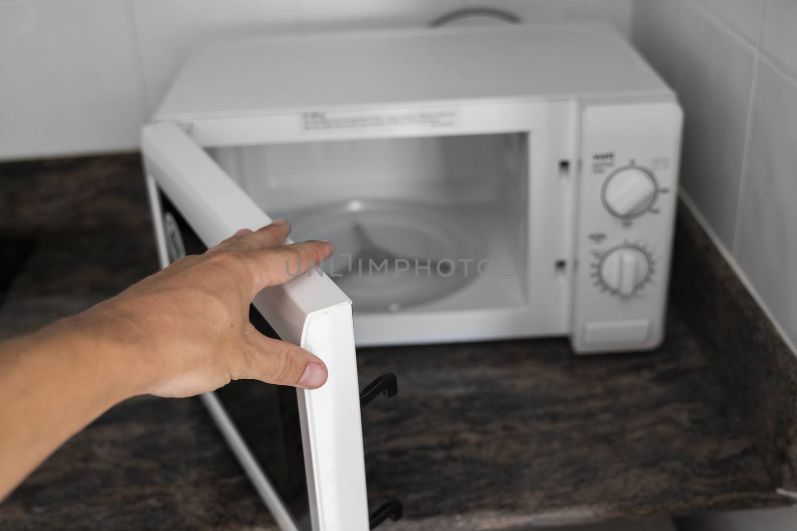 Man hand holdind a door of microwave in a kitchen for cooking or heating a dish. by vovsht