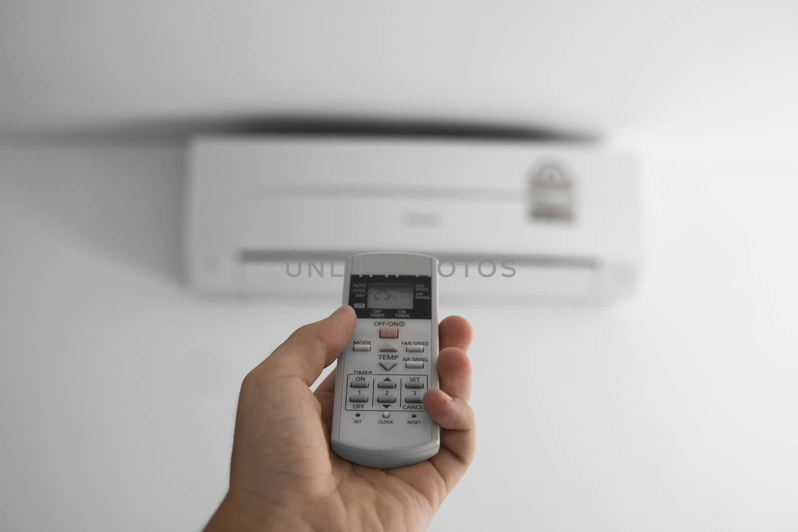 Man's hand using remote controler. Hand holding rc and adjusting temperature of air conditioner mounted on a white wall. Indooor comfort temperature. Health concepts and energy savings. by vovsht