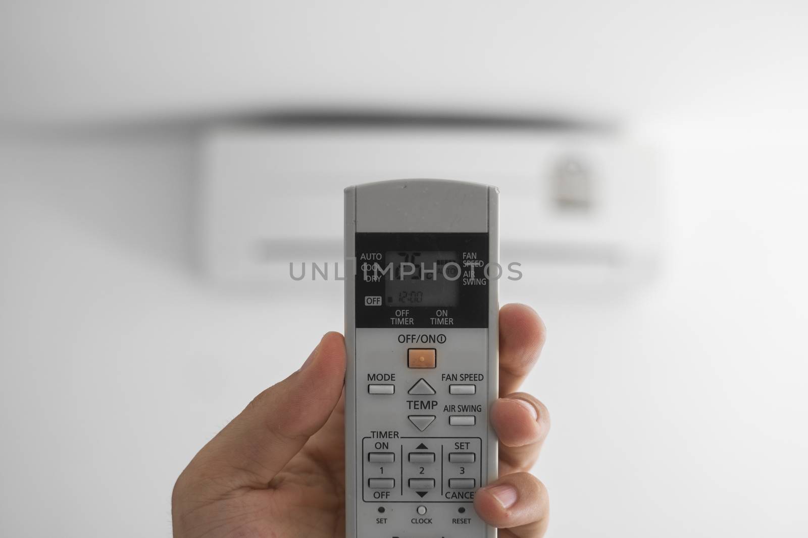 Man's hand using remote controler. Hand holding rc and adjusting temperature of air conditioner mounted on a white wall. Indooor comfort temperature. Health concepts and energy savings. by vovsht