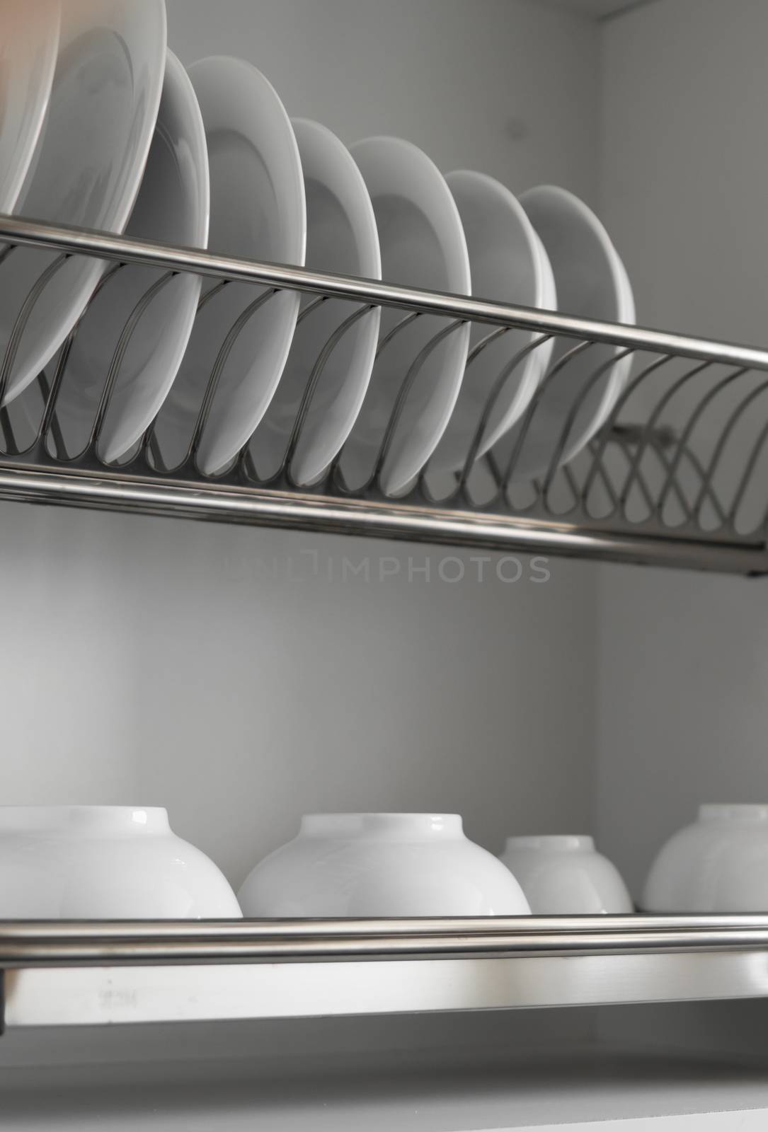 Dish drying metal rack with big nice white clean plates. Traditional comfortable kitchen. Open white dish draining closet with wet dishes of glass and ceramic, plates, bowls drying inside on rack