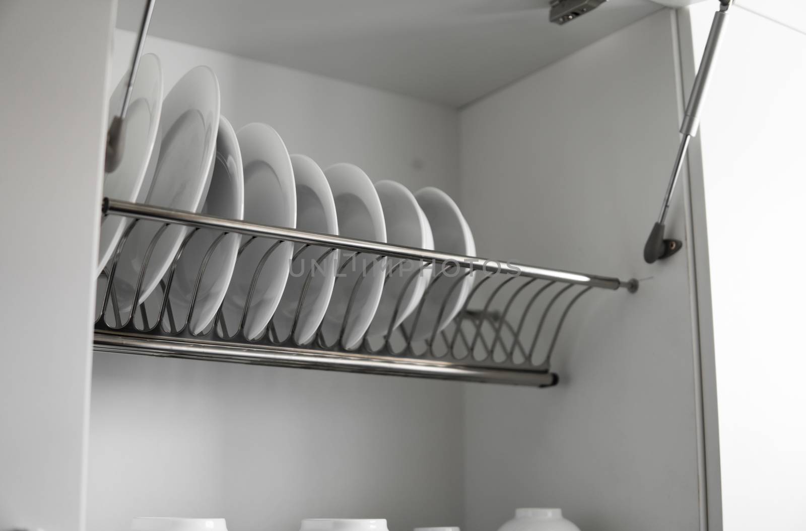 Dish drying metal rack with big nice white clean plates. Traditional comfortable kitchen. Open white dish draining closet with wet dishes of glass and ceramic, plates, bowls drying inside on rack
