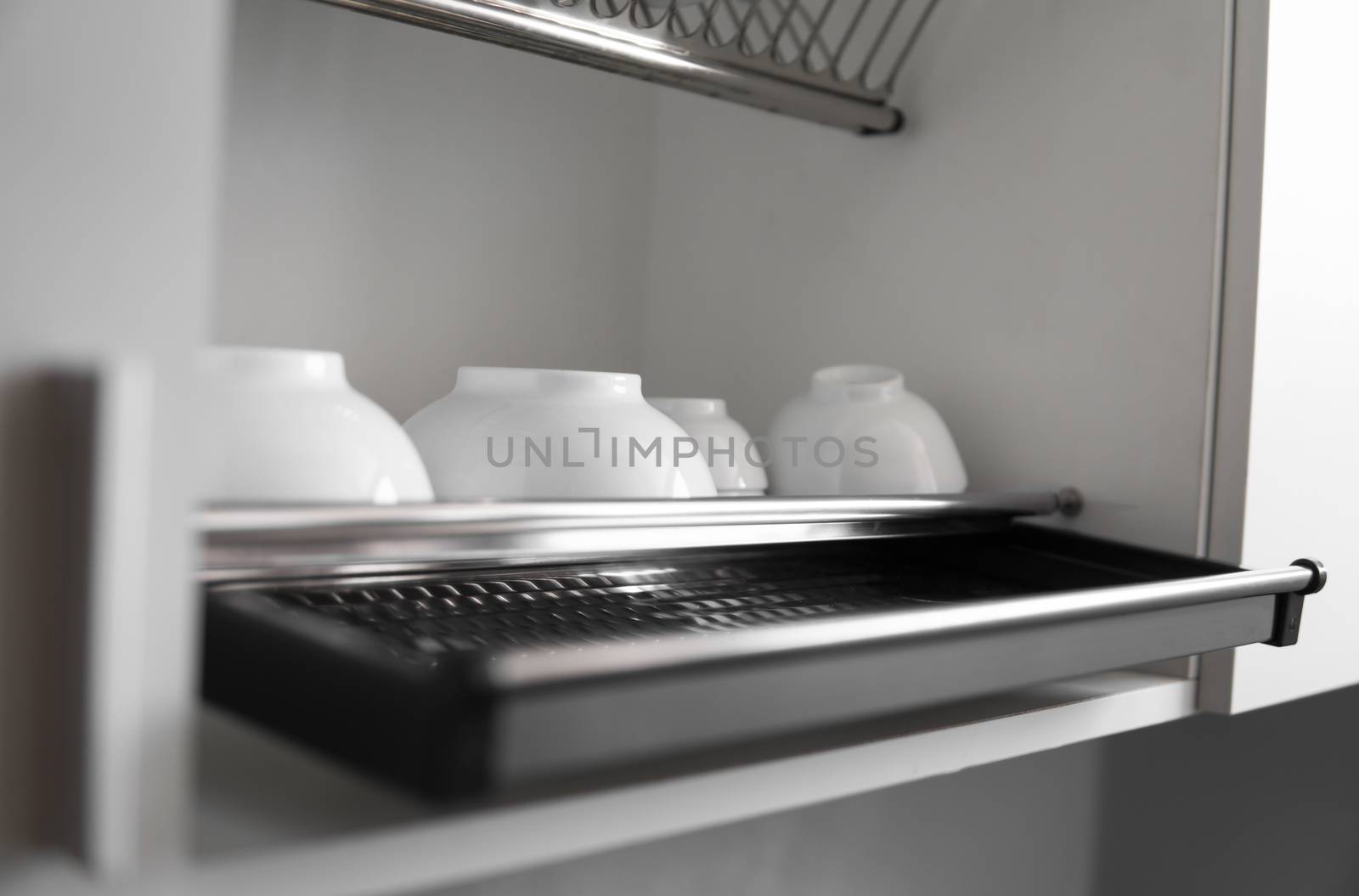 Dish drying metal rack with big nice white clean plates. Traditional comfortable kitchen. Open white dish draining closet with wet dishes of glass and ceramic, plates, bowls drying inside on rack
