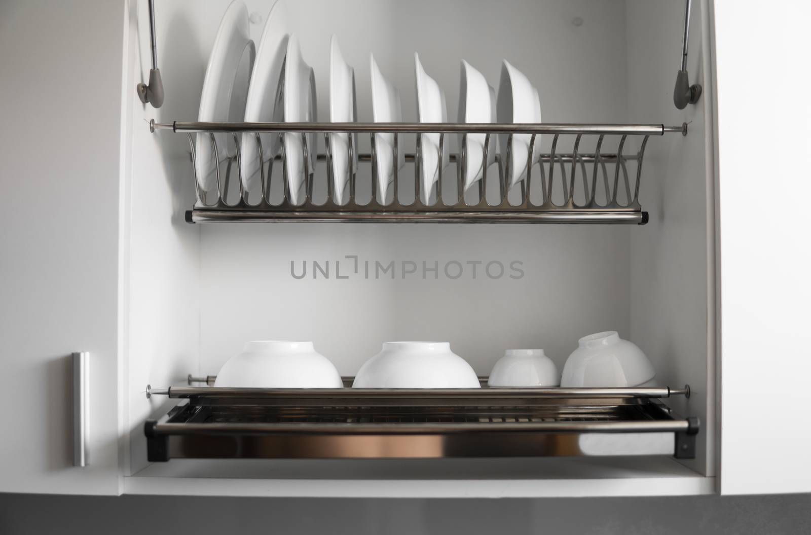 Dish drying metal rack with big nice white clean plates. Traditional comfortable kitchen. Open white dish draining closet with wet dishes of glass and ceramic, plates, bowls drying inside on rack. by vovsht