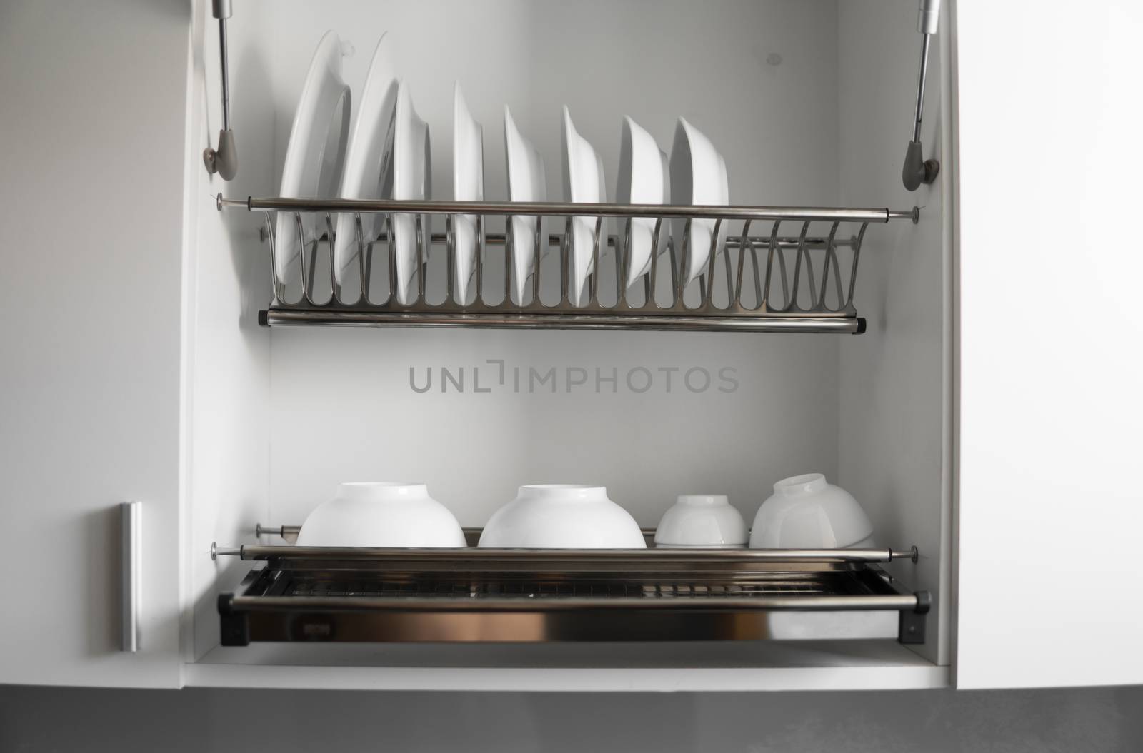 Dish drying metal rack with big nice white clean plates. Traditional comfortable kitchen. Open white dish draining closet with wet dishes of glass and ceramic, plates, bowls drying inside on rack