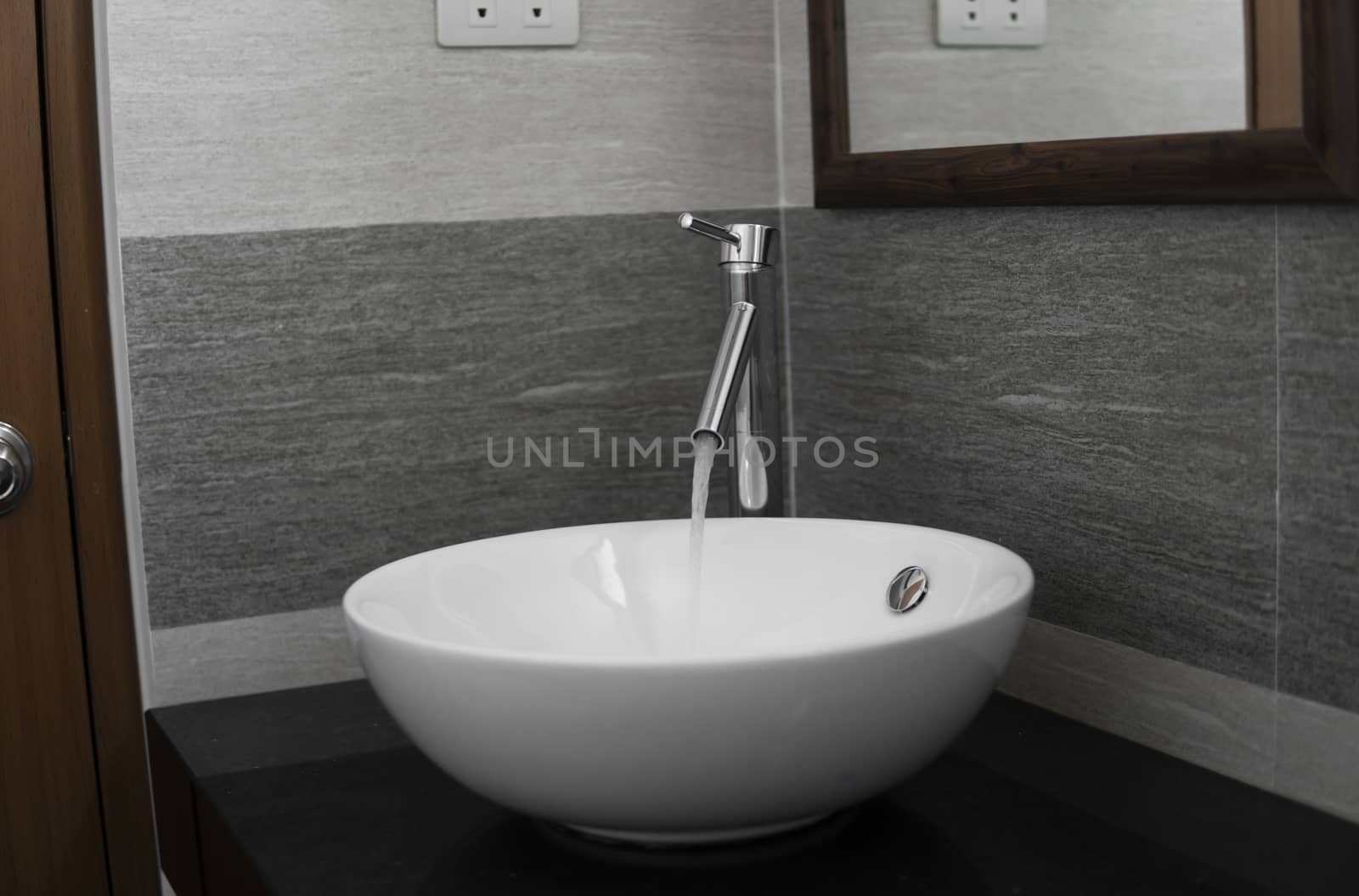 Bathroom interior with white round sink and chrome faucet in a modern bathroom. Water flowing from the chrome faucet