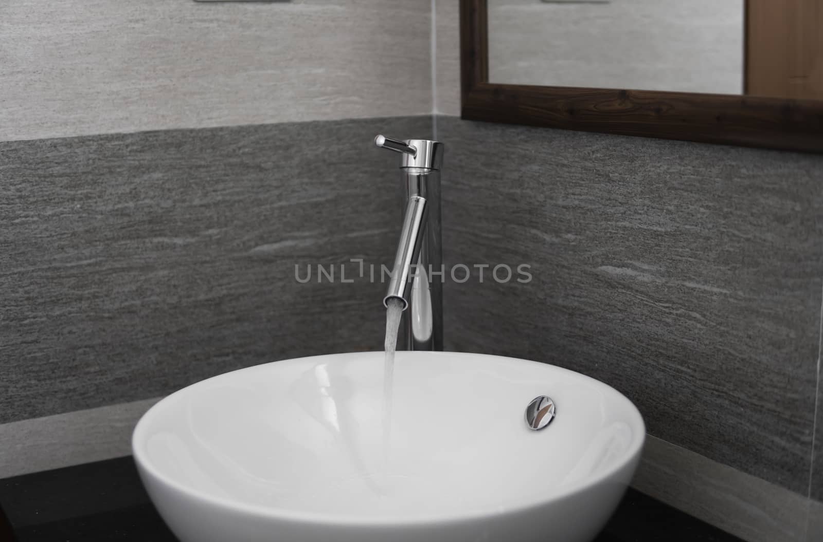 Bathroom interior with white round sink and chrome faucet in a modern bathroom. Water flowing from the chrome faucet