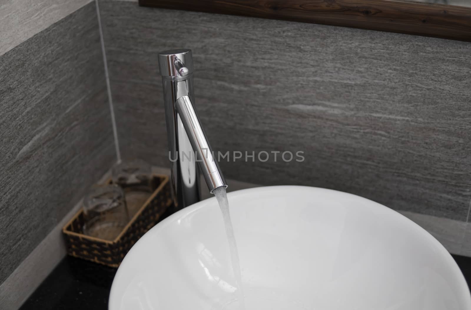 Bathroom interior with white round sink and chrome faucet in a modern bathroom. Water flowing from the chrome faucet