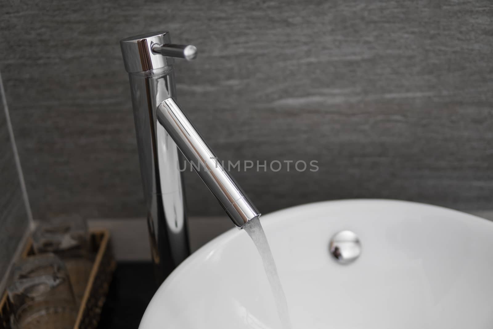 Bathroom interior with white round sink and chrome faucet in a modern bathroom. Water flowing from the chrome faucet