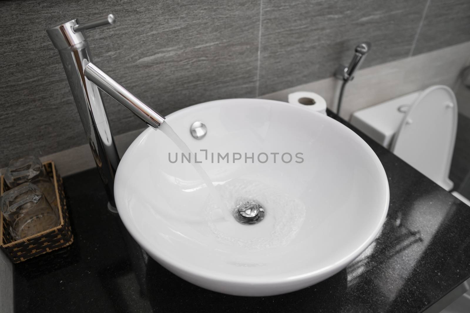 Bathroom interior with white round sink and chrome faucet in a modern bathroom. Water flowing from the chrome faucet. by vovsht