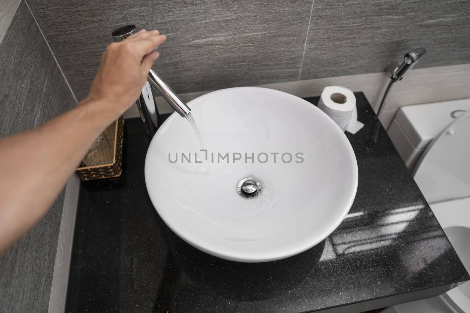 Male hand use a faucet in a bathroom interior with white round sink and chrome faucet. Water flowing from the chrome faucet